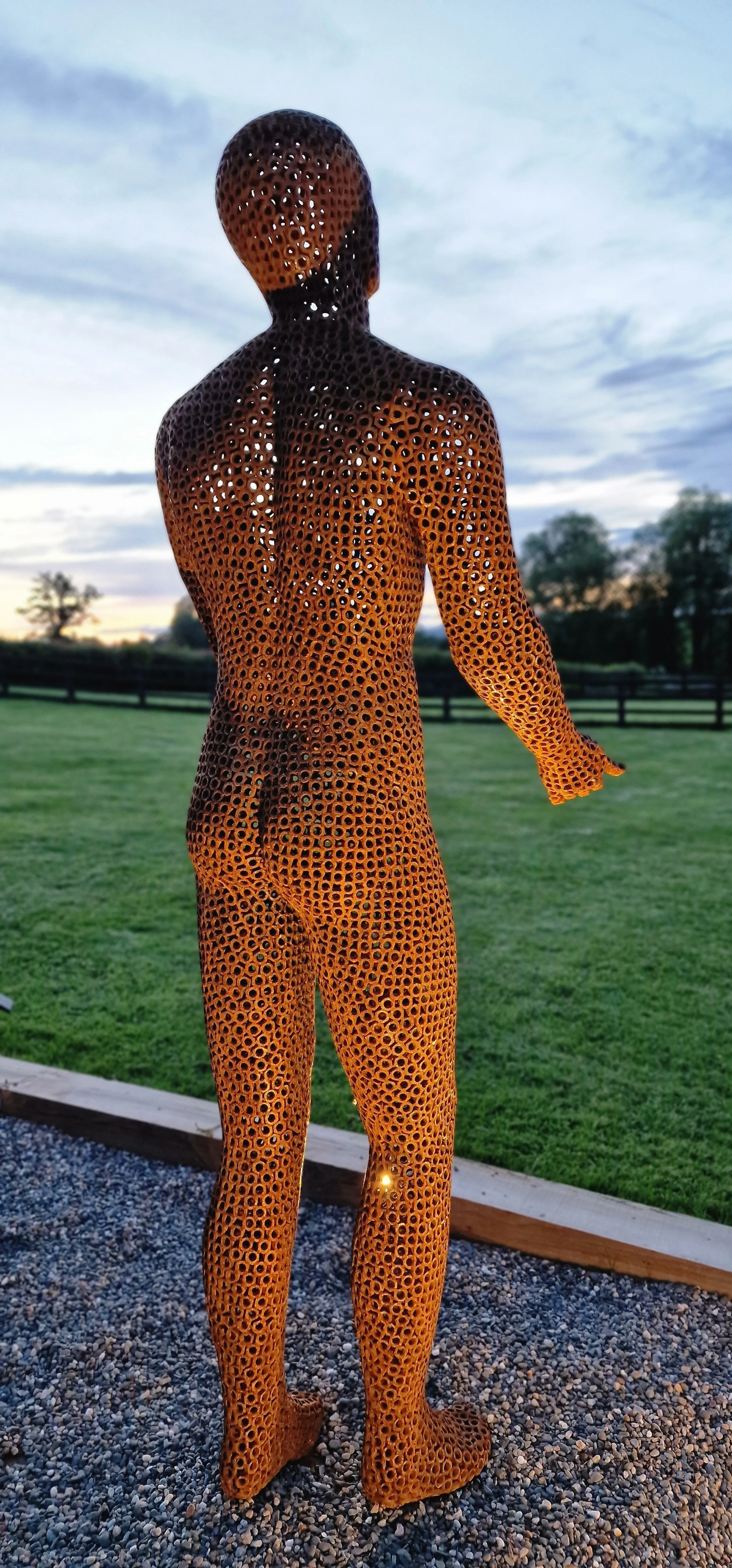 This is a life-size metal sculpture made from nuts depicting a man looking up into the sky with his hands held out in front of him trying to fill the rain