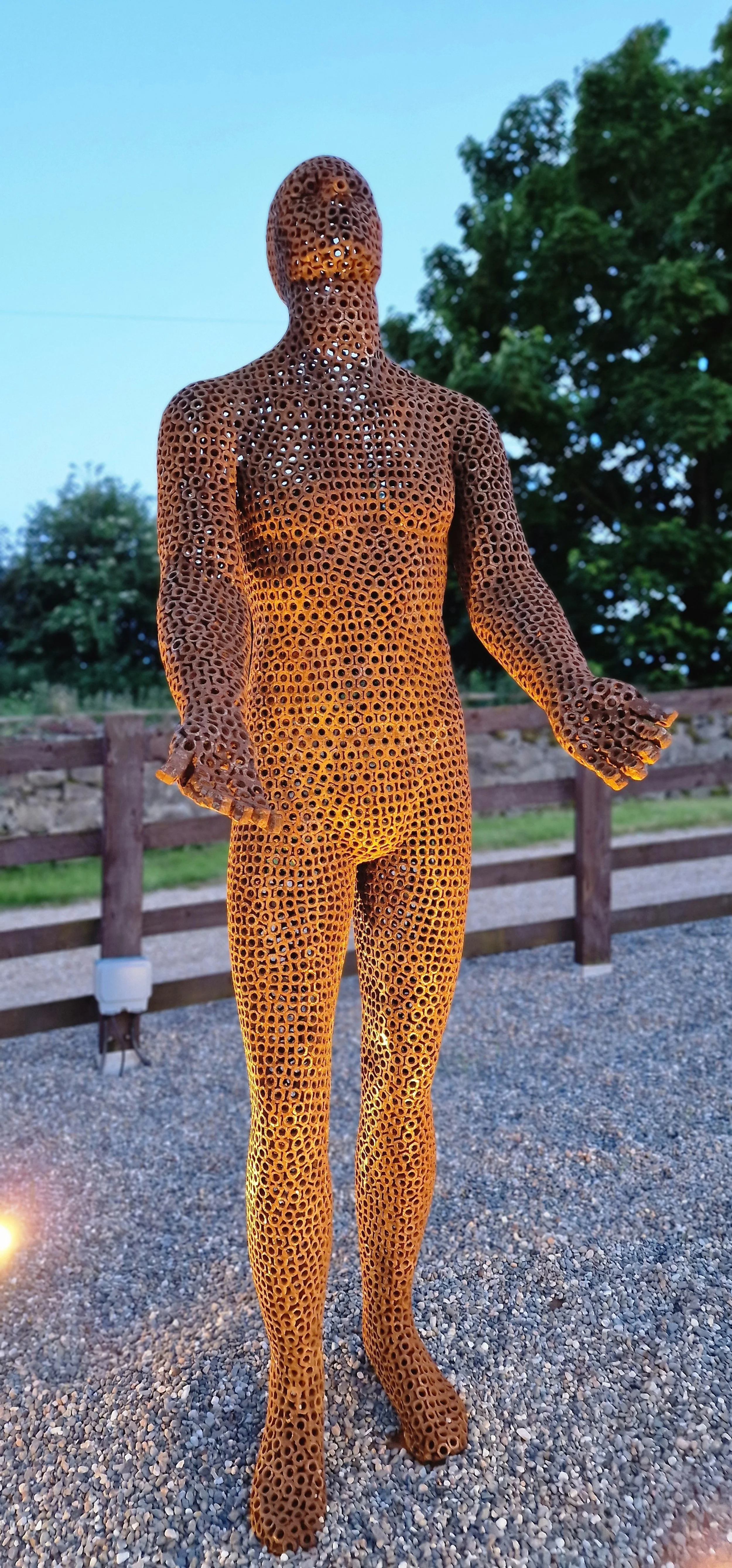This is a life-size metal sculpture made from nuts depicting a man looking up into the sky with his hands held out in front of him trying to fill the rain