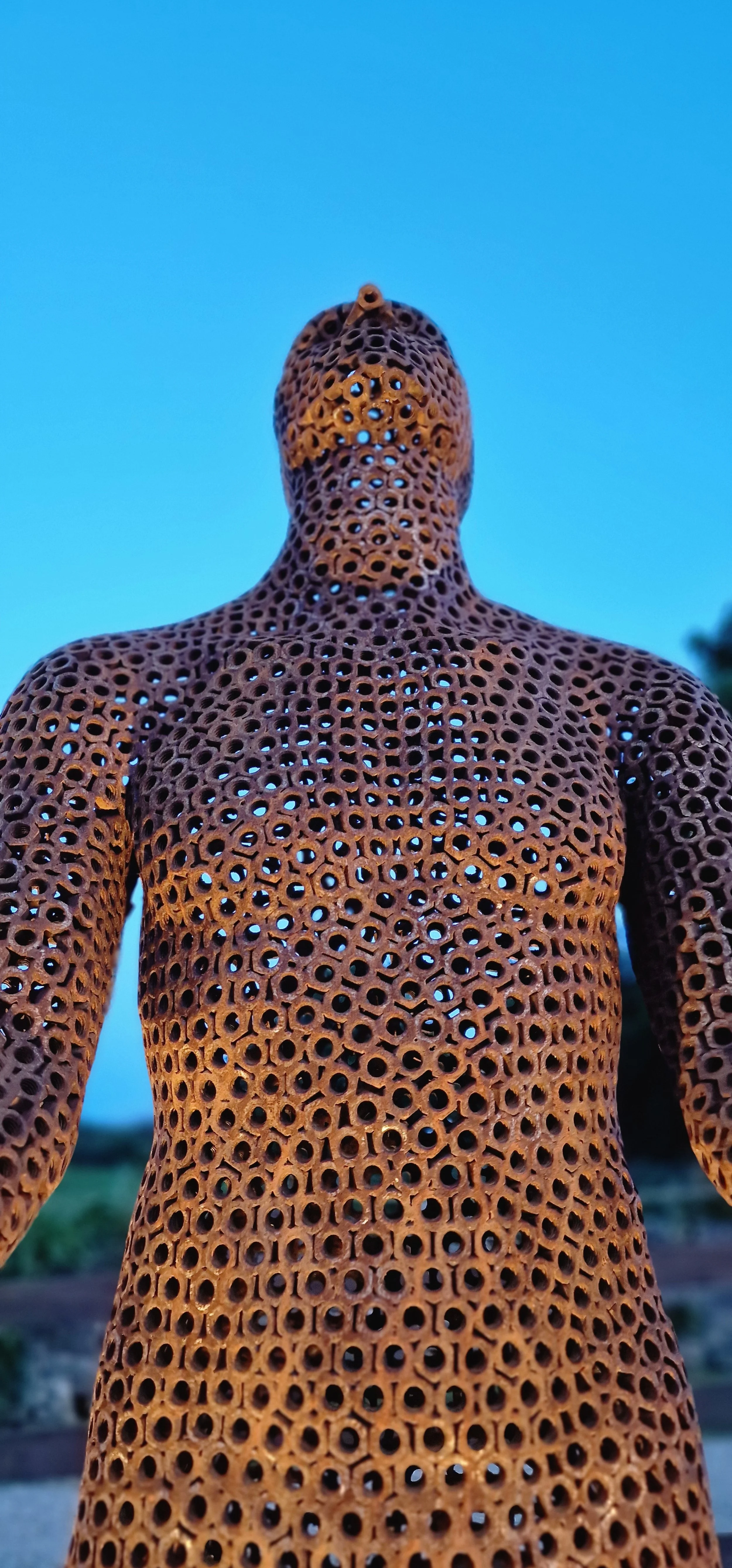 This is a life-size metal sculpture made from nuts depicting a man looking up into the sky with his hands held out in front of him trying to fill the rain