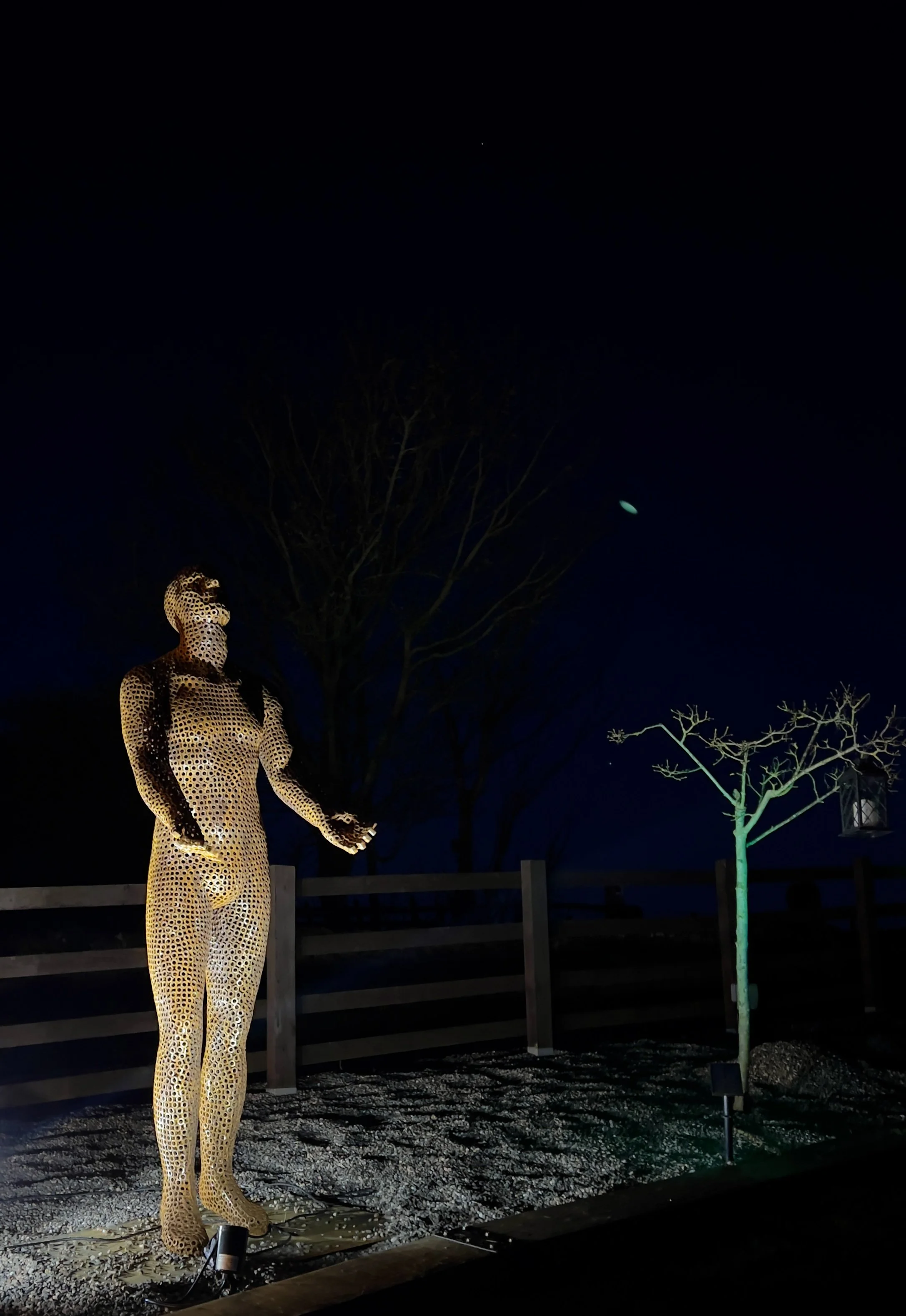 This is a life-size metal sculpture made from nuts depicting a man looking up into the sky with his hands held out in front of him trying to fill the rain