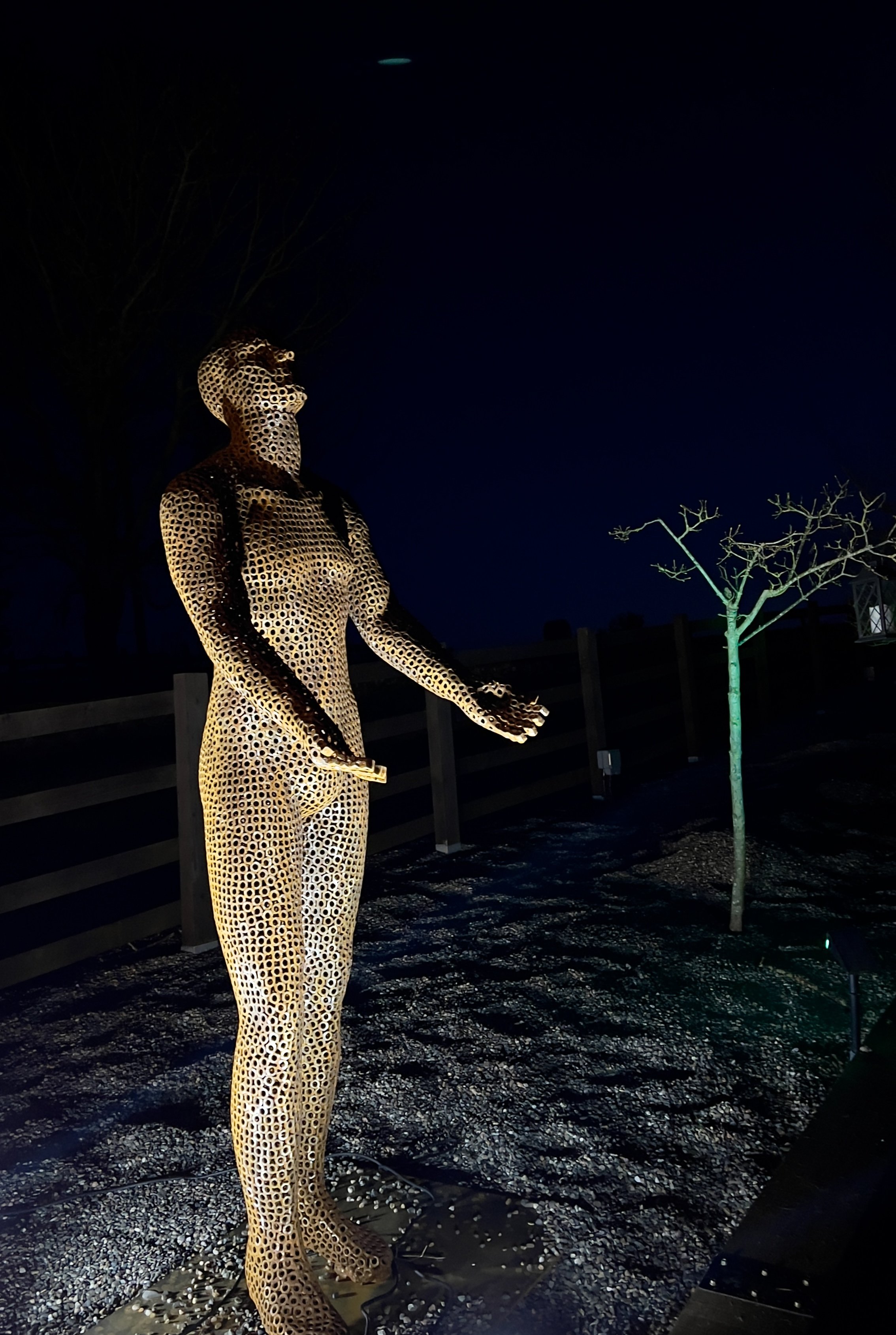 This is a life-size metal sculpture made from nuts depicting a man looking up into the sky with his hands held out in front of him trying to fill the rain