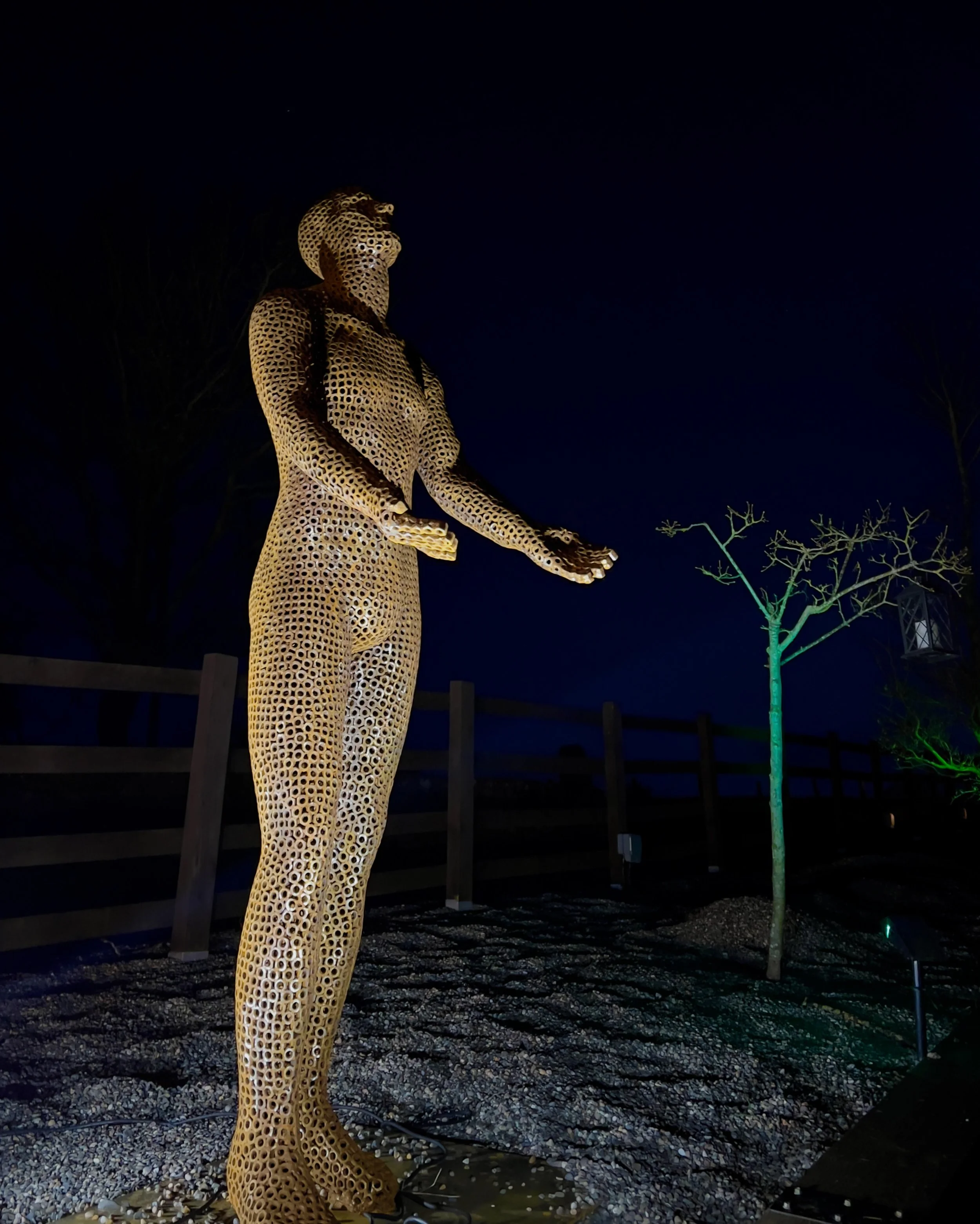 This is a life-size metal sculpture made from nuts depicting a man looking up into the sky with his hands held out in front of him trying to fill the rain
