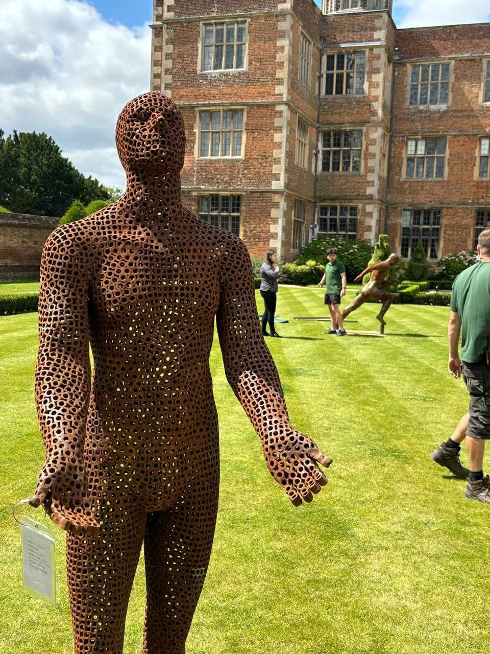 This is a life-size metal sculpture made from nuts depicting a man looking up into the sky with his hands held out in front of him trying to fill the rain