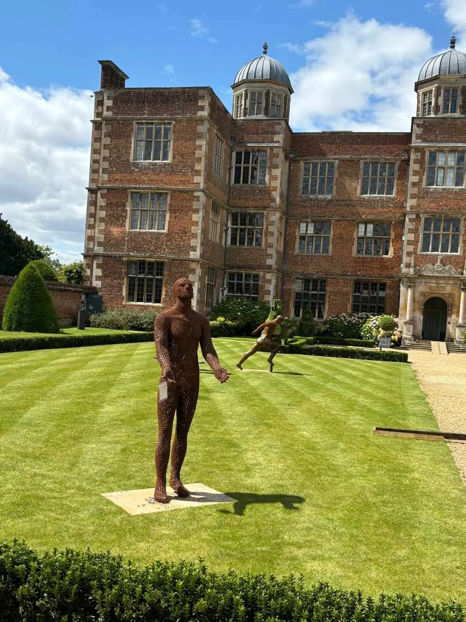 This is a life-size metal sculpture made from nuts depicting a man looking up into the sky with his hands held out in front of him trying to fill the rain