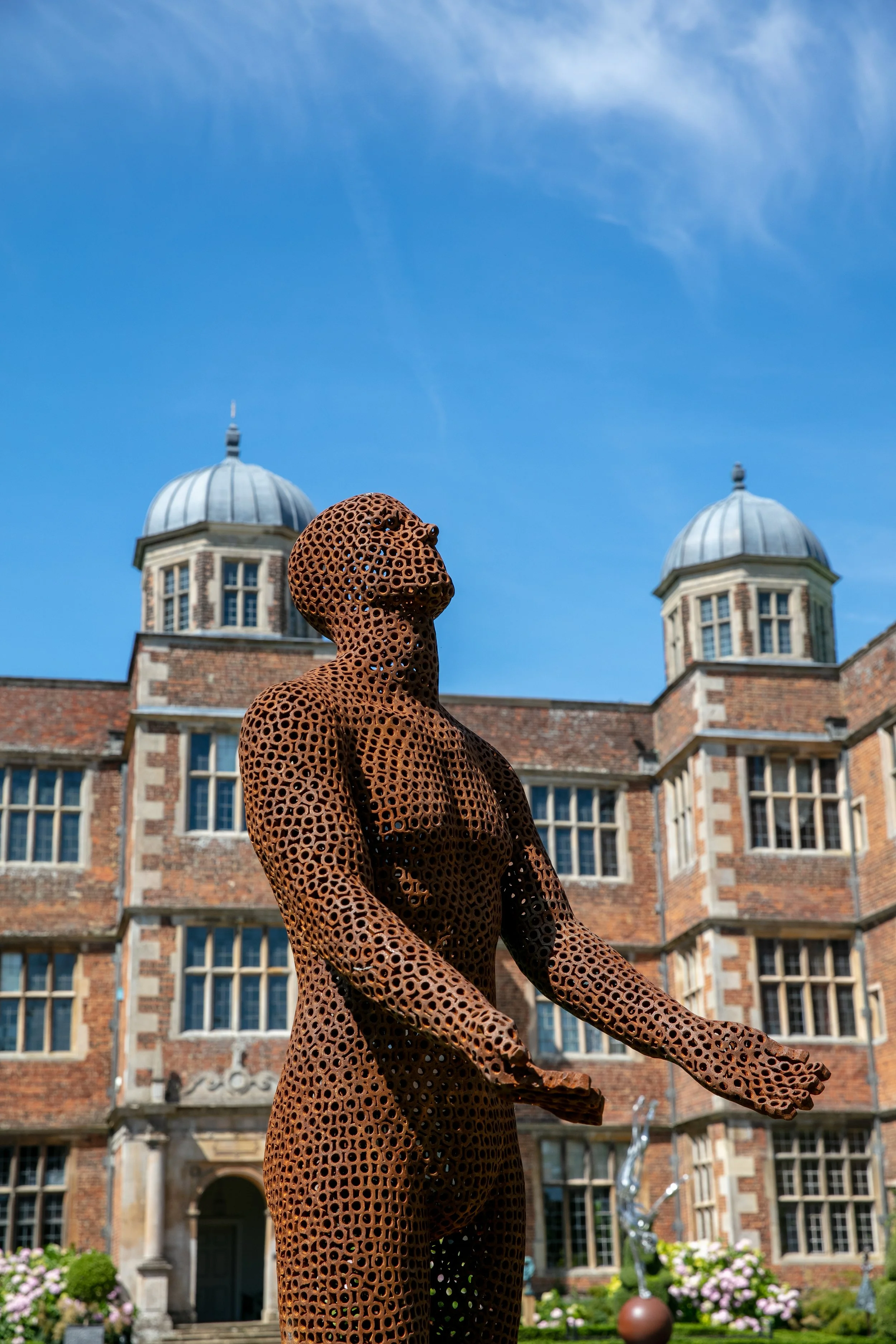 This is a life-size metal sculpture made from nuts depicting a man looking up into the sky with his hands held out in front of him trying to fill the rain