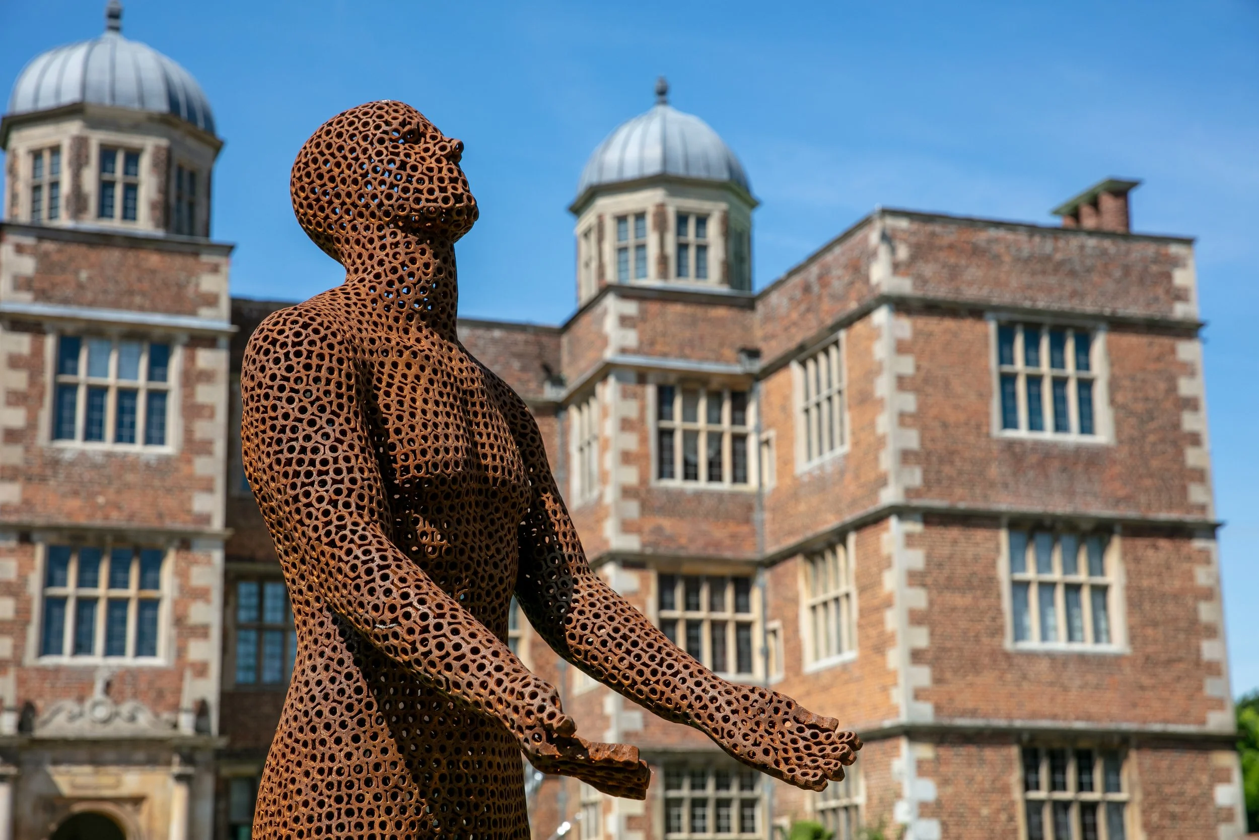 This is a life-size metal sculpture made from nuts depicting a man looking up into the sky with his hands held out in front of him trying to fill the rain