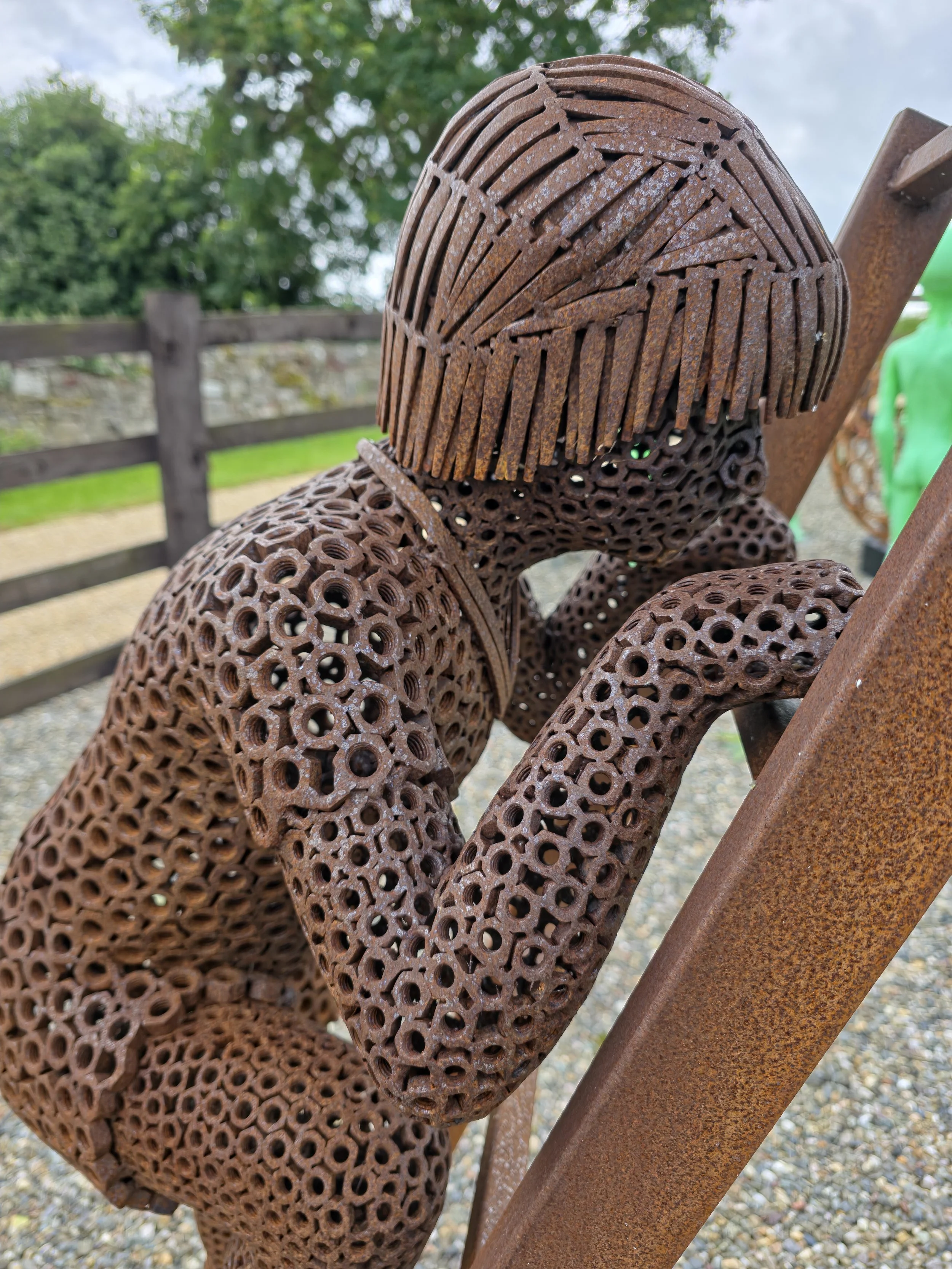 Boy climbing ladder sculpture — “Hand‑crafted steel sculpture by Shaun Gagg showing a small boy climbing a ladder, made from welded nuts with handmade nail hair.”