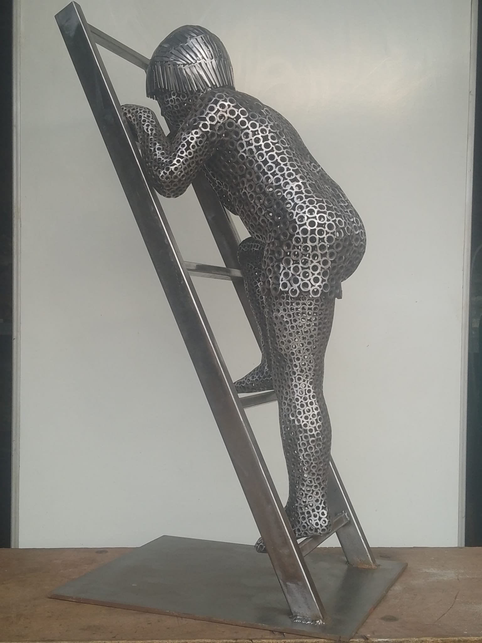 Hand‑made metal art — “Hand‑made metal sculpture of a boy on a ladder, built from steel nuts and nails, finished in raw silver steel.”
