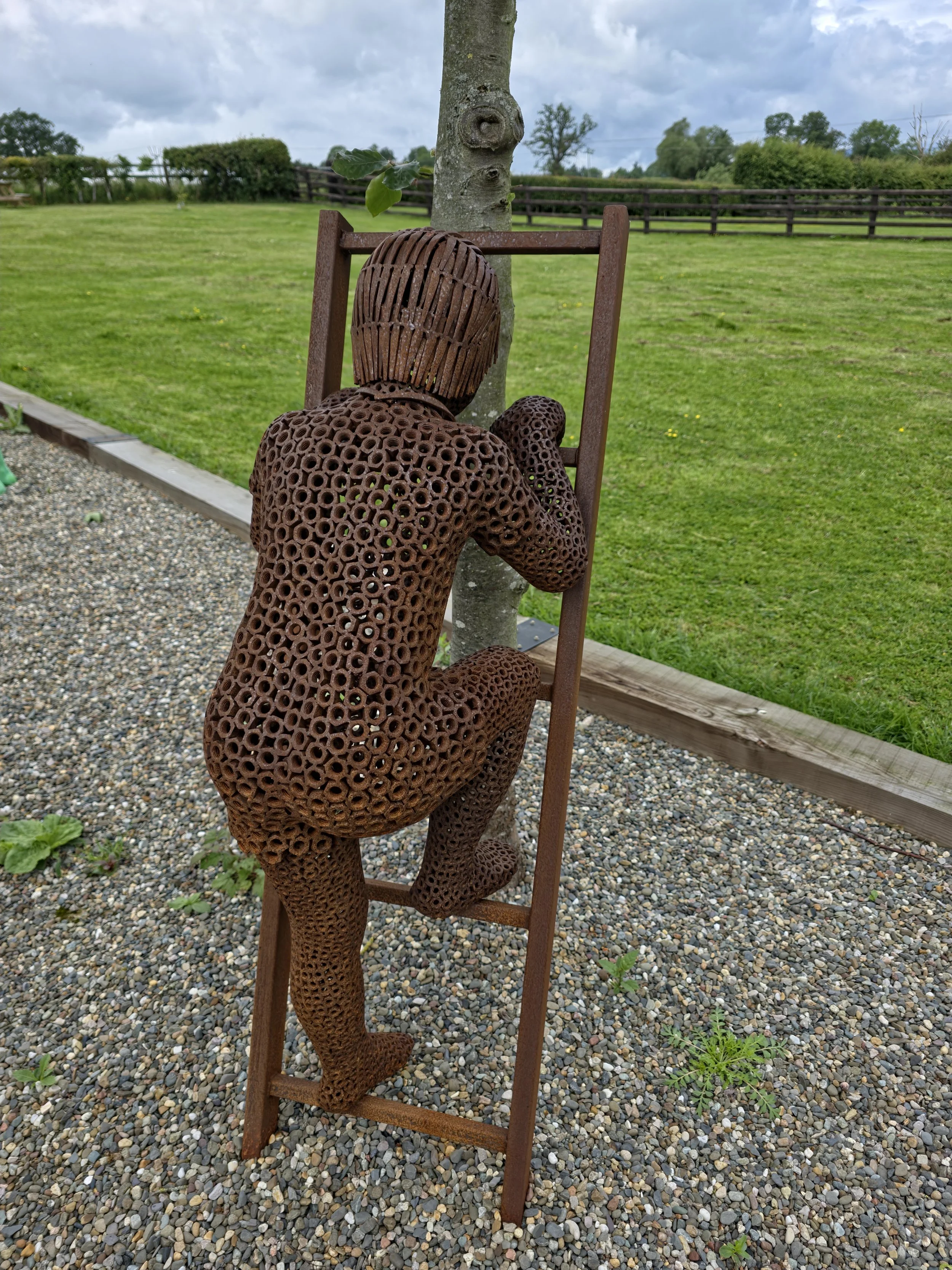 Climbing boy metal figure — “Metal sculpture of a child climbing a ladder, made from welded nuts with individually placed handmade nails for hair.”