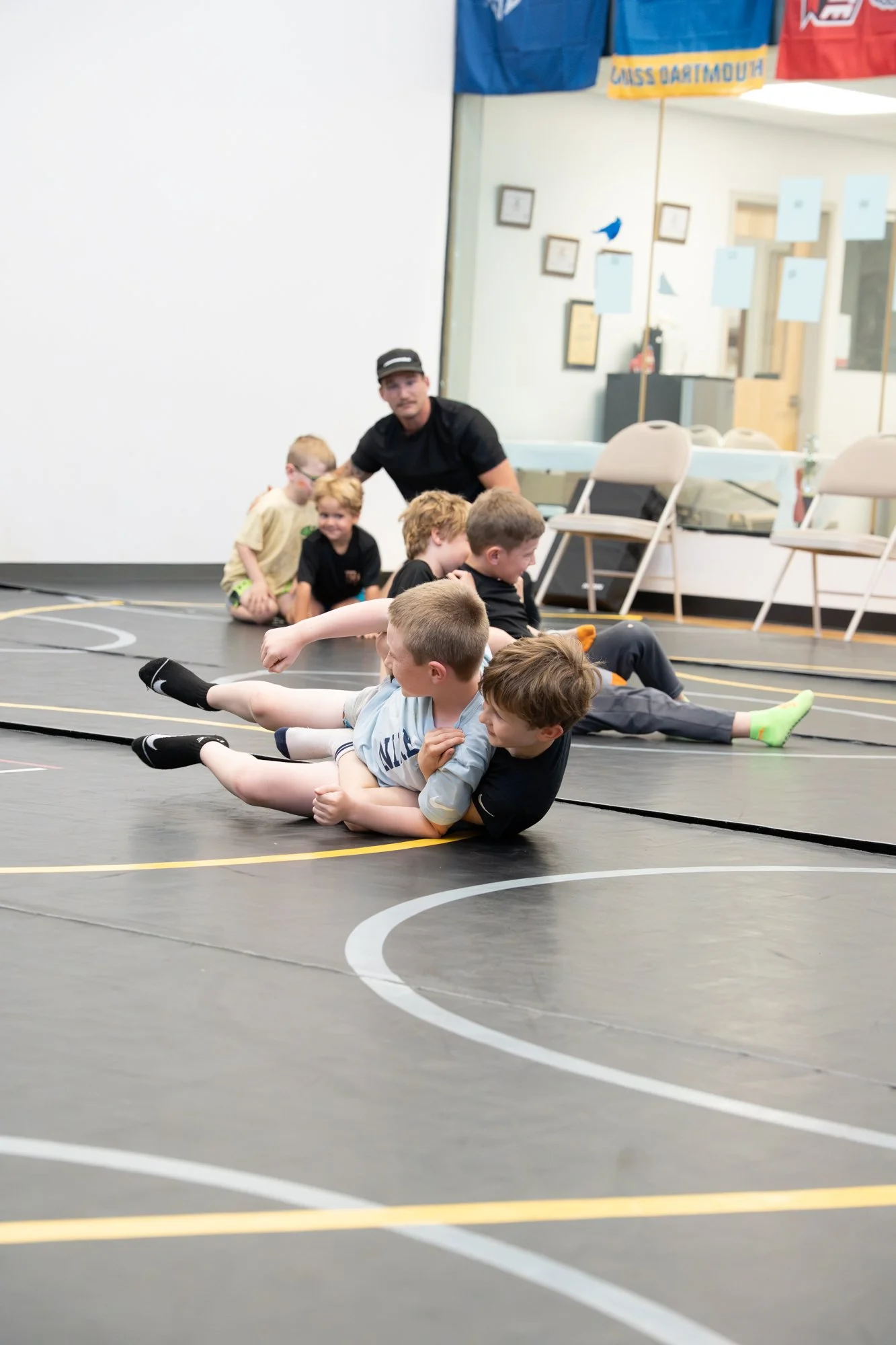 Children participating in a wrestling activity on a gym mat, supervised by an adult.