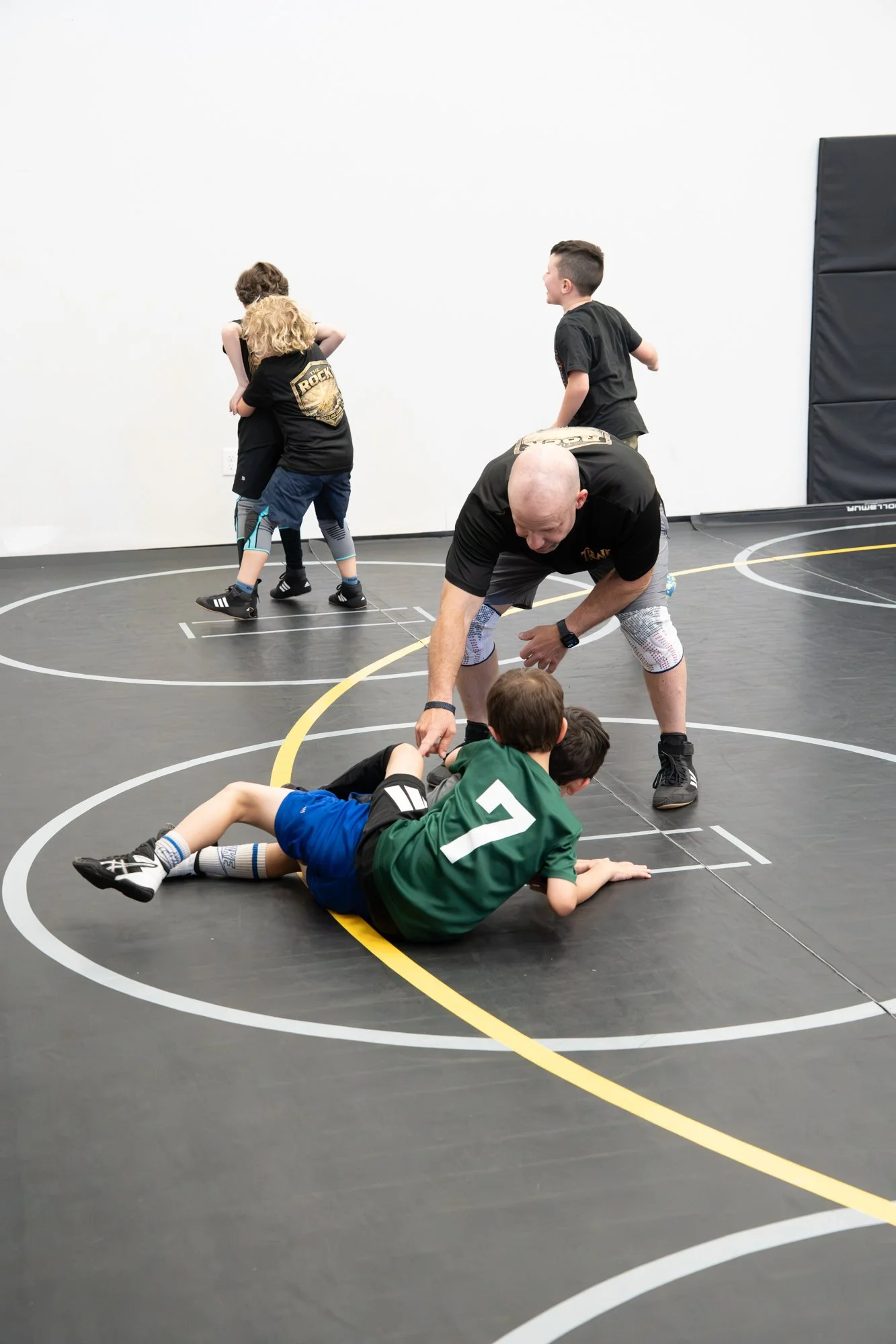 Children and adults participating in a wrestling practice on a gym mat.