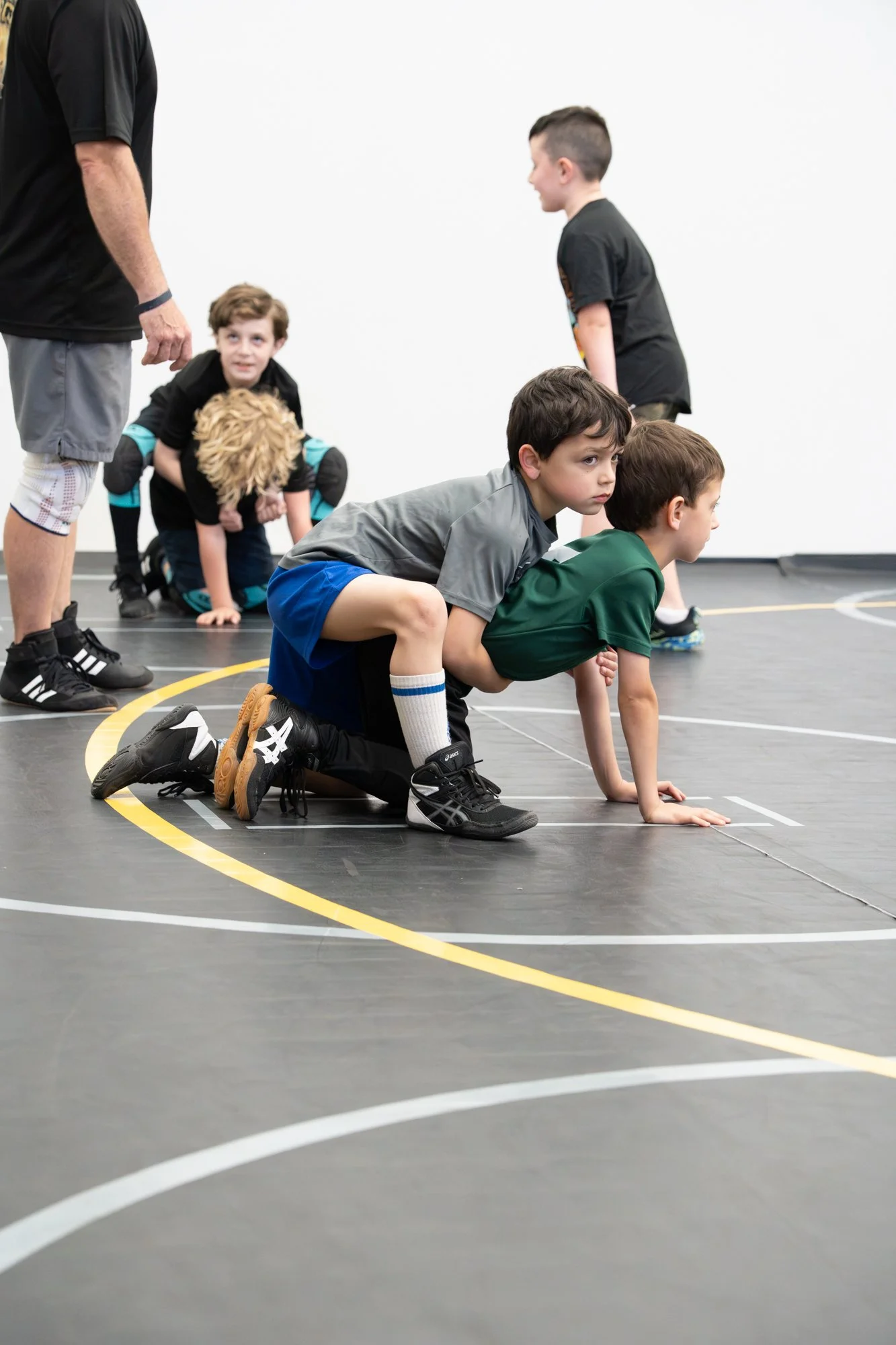 Children in a gymnasium participating in a crawling race, with some children on their hands and knees and a coach or instructor standing nearby.