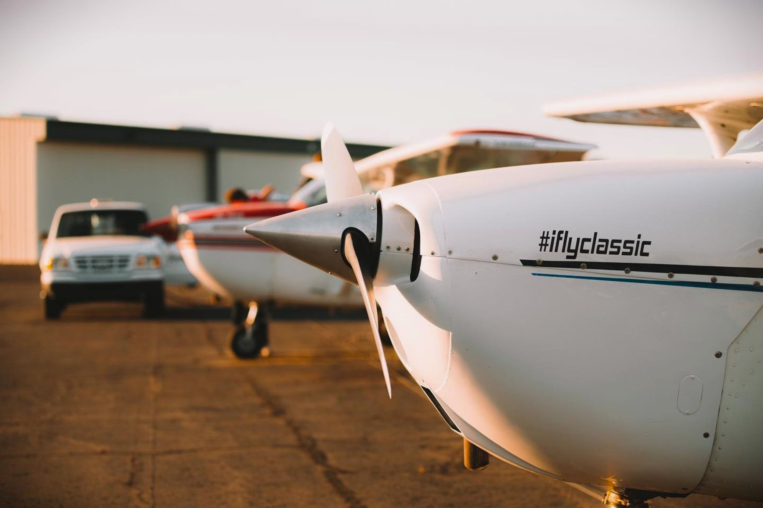 Small private jet parked on the tarmac with other aircraft in the background during sunset