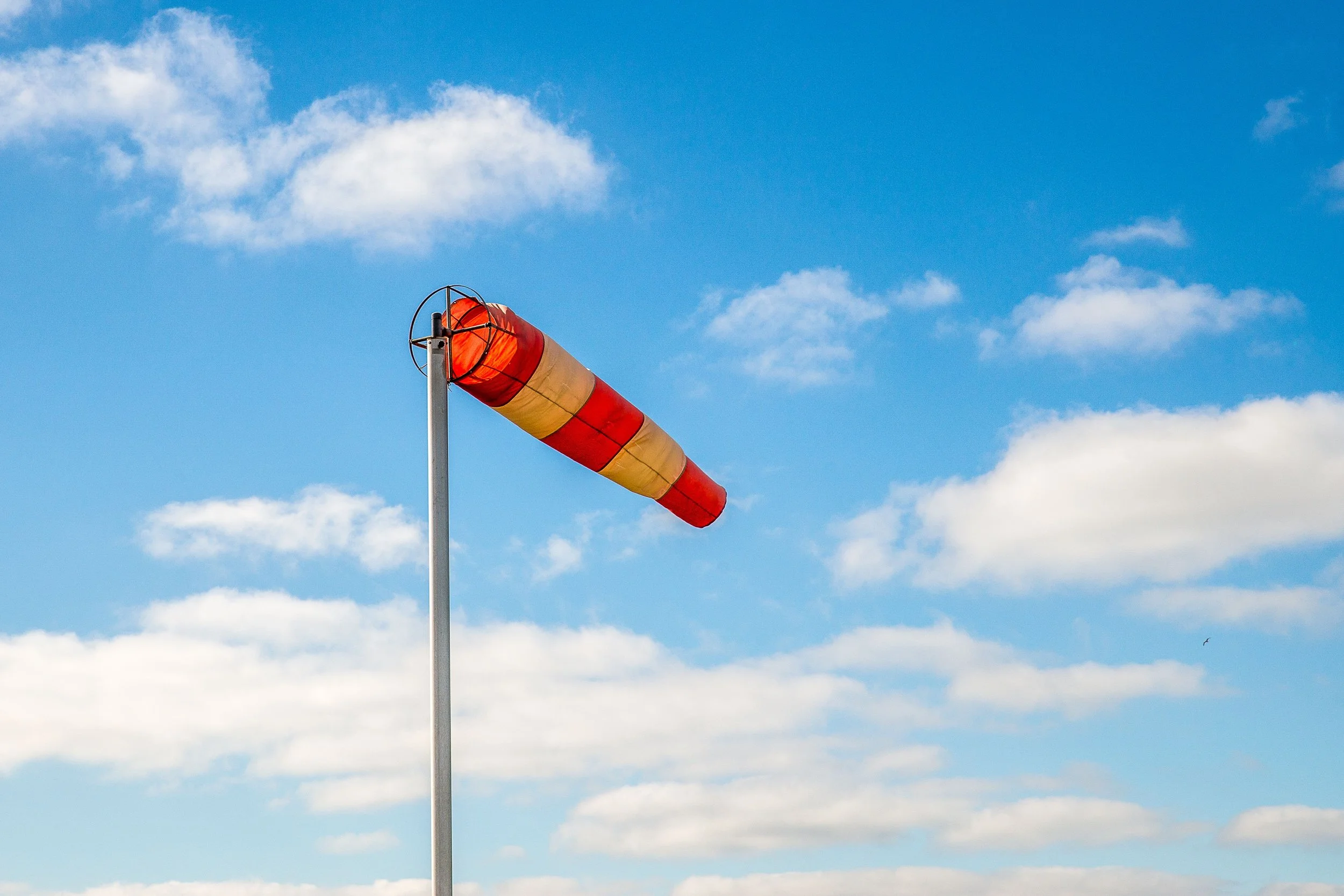 Orange and yellow windsock blowing in the wind against a blue sky with scattered clouds.