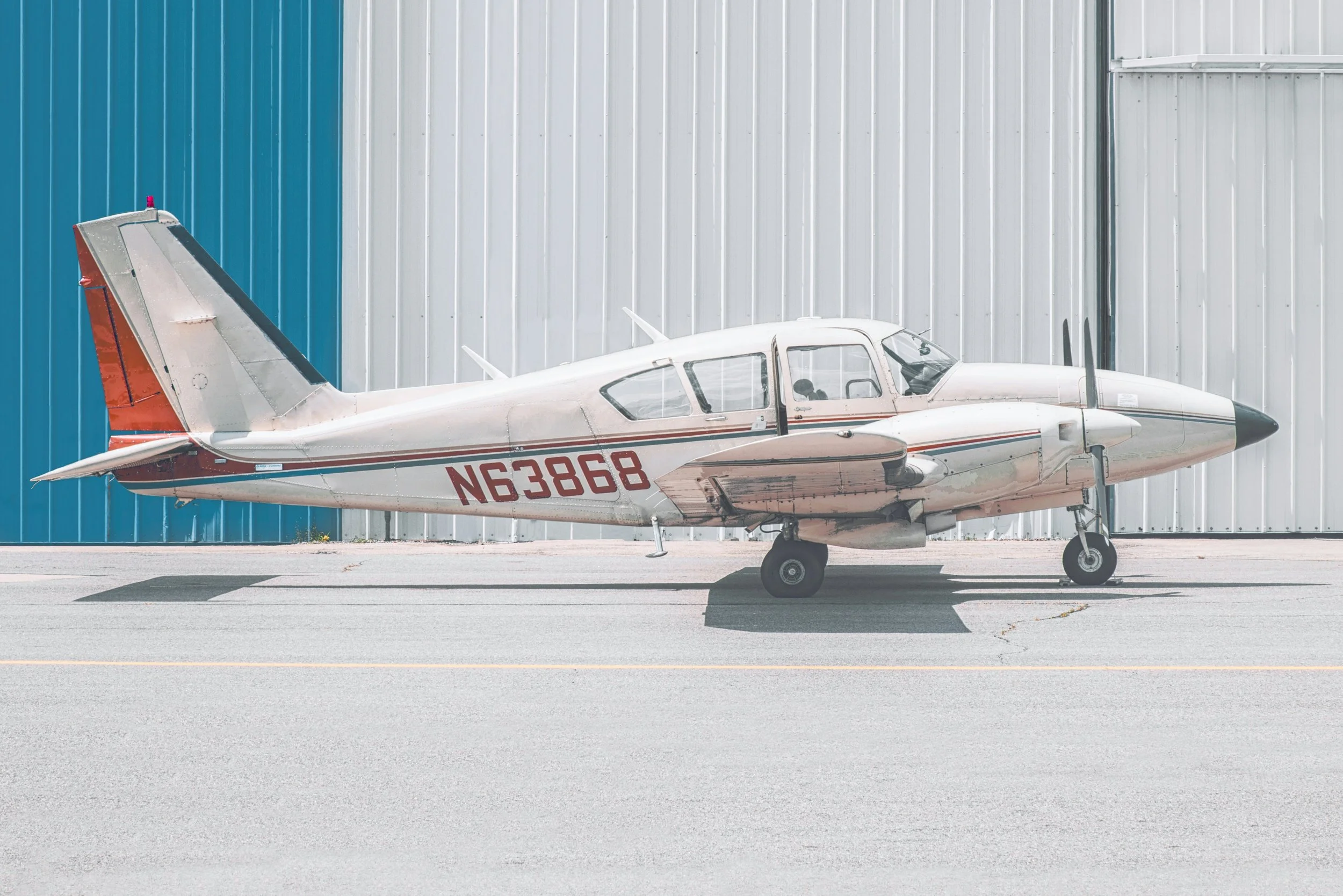 Small white and red private jet parked on tarmac in front of a large silver and blue hangar.