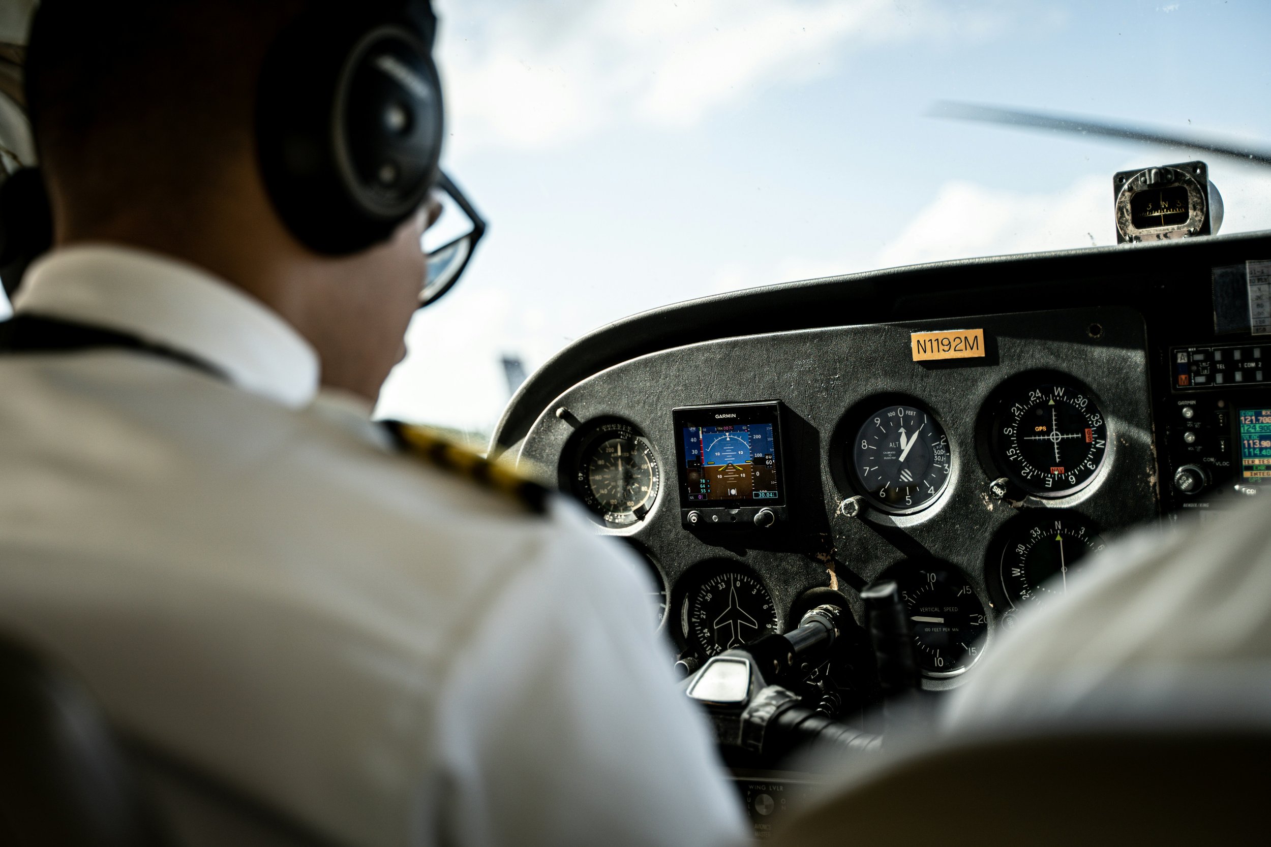 Pilot in the cockpit of an airplane, looking at the instrument panel with gauges and navigational equipment, with a clear sky outside.