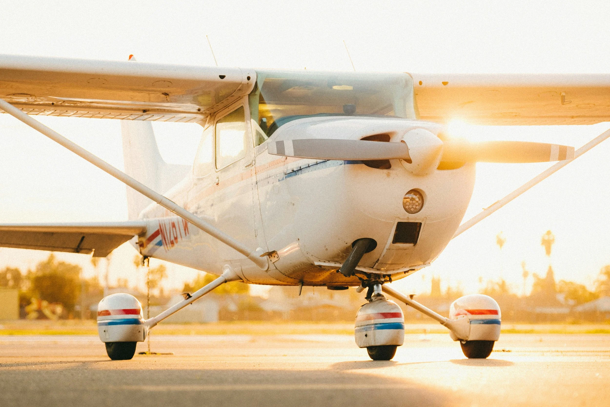 Small white airplane with a high wing design and a tricycle landing gear, parked on a runway at sunset.