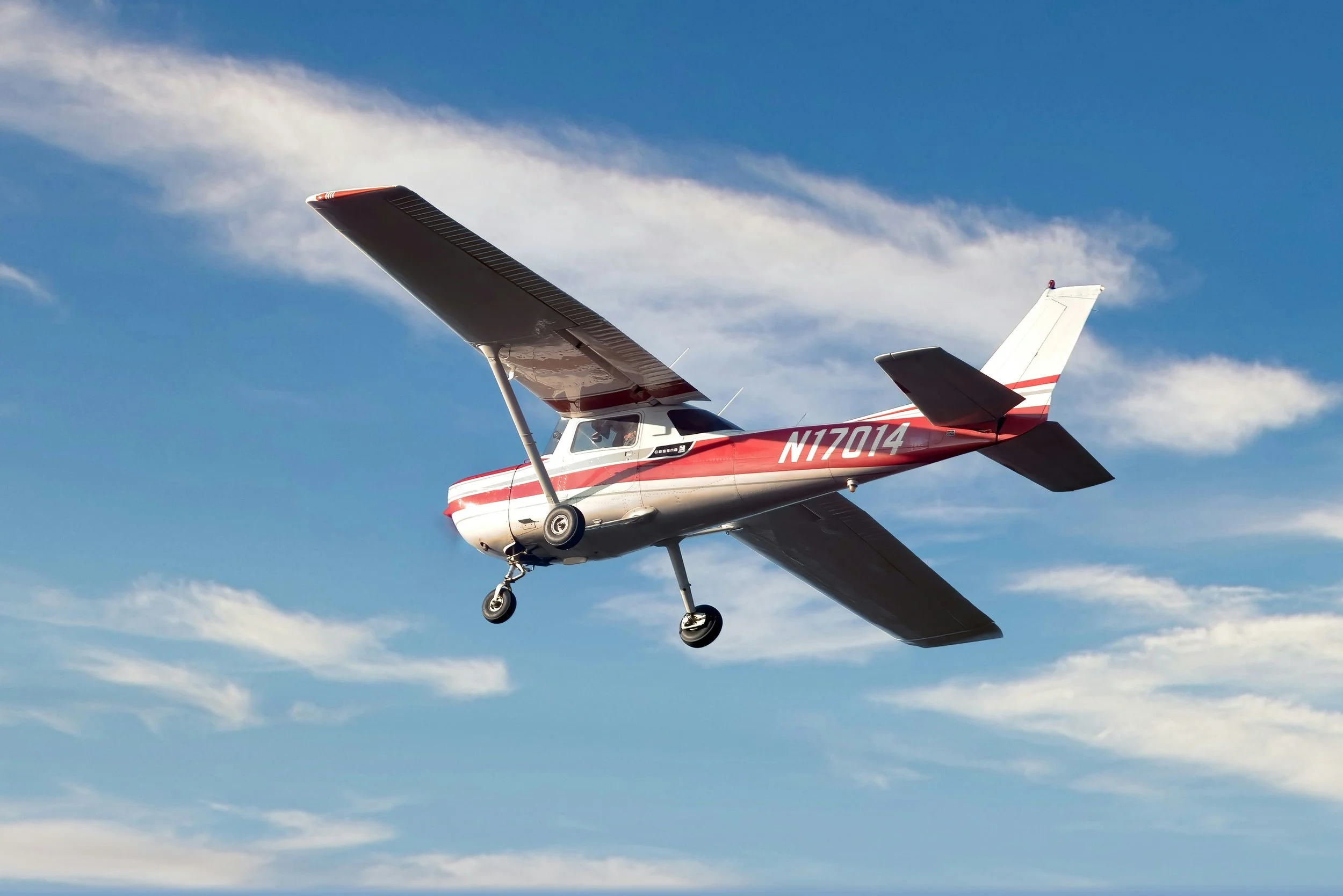A small red and white airplane flying in a blue sky with a few clouds.