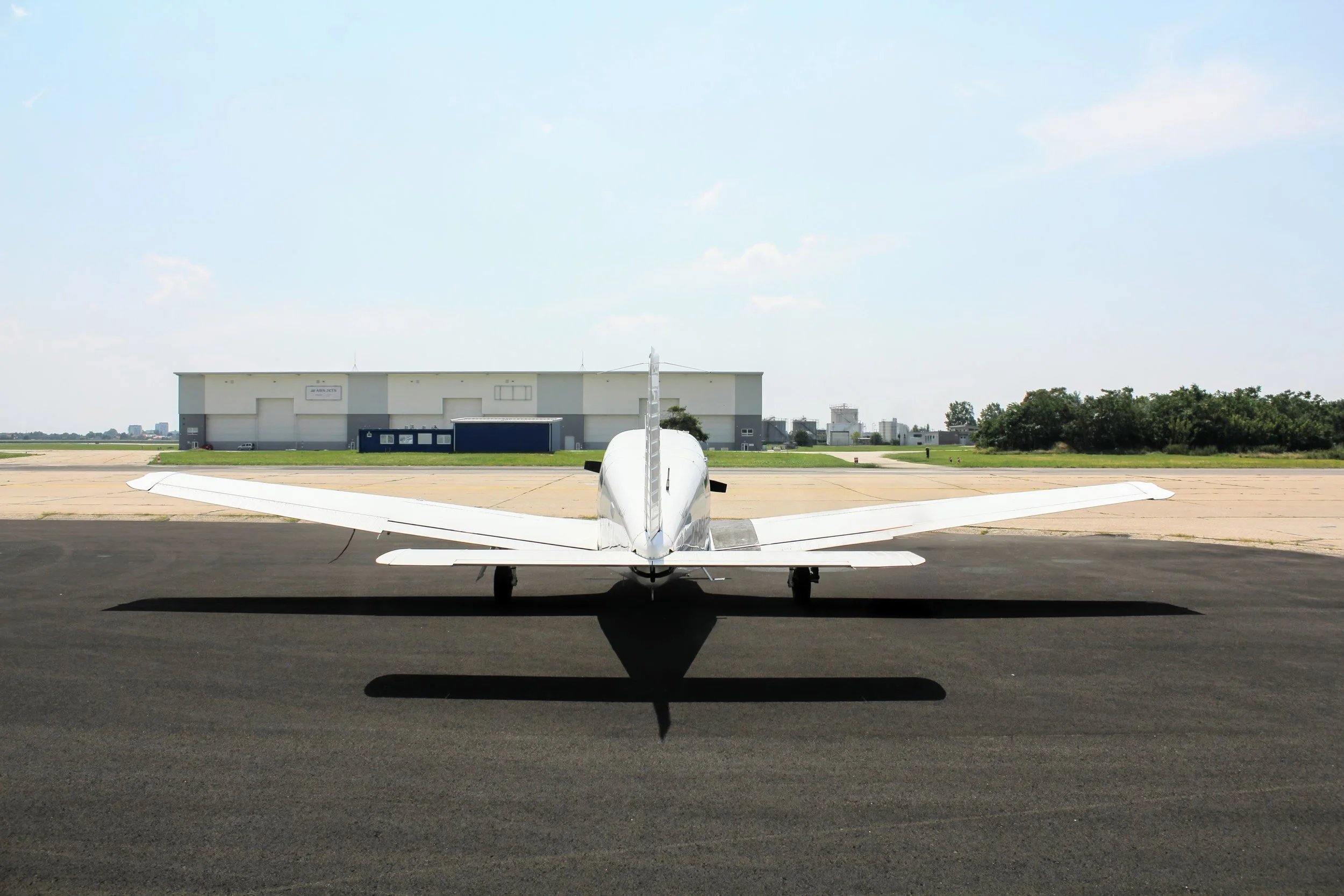 Small white airplane on runway with hangar and cityscape in background, clear sky.