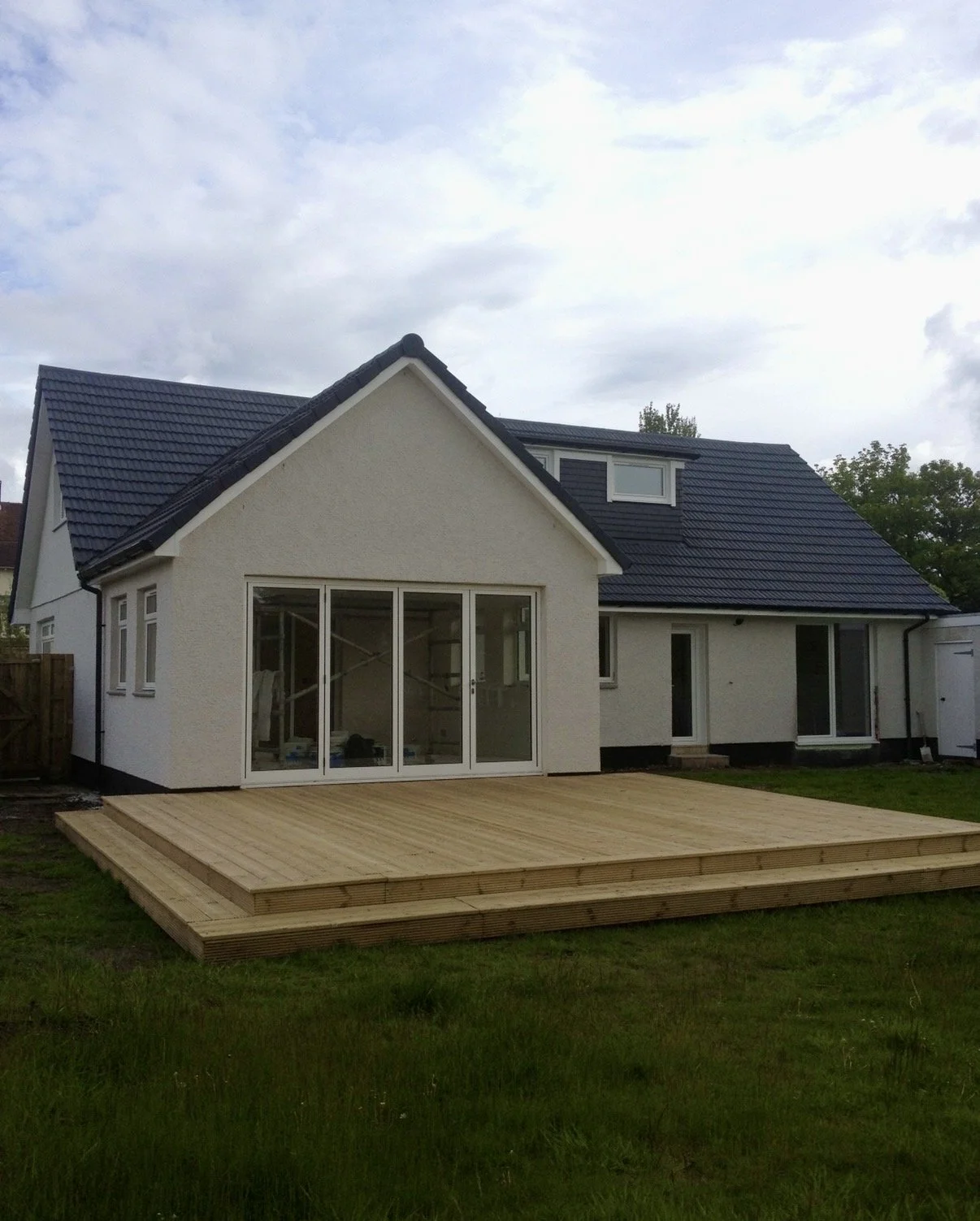 A house with white exterior walls, a dark blue roof, and large glass sliding doors opening onto a wooden deck in the backyard