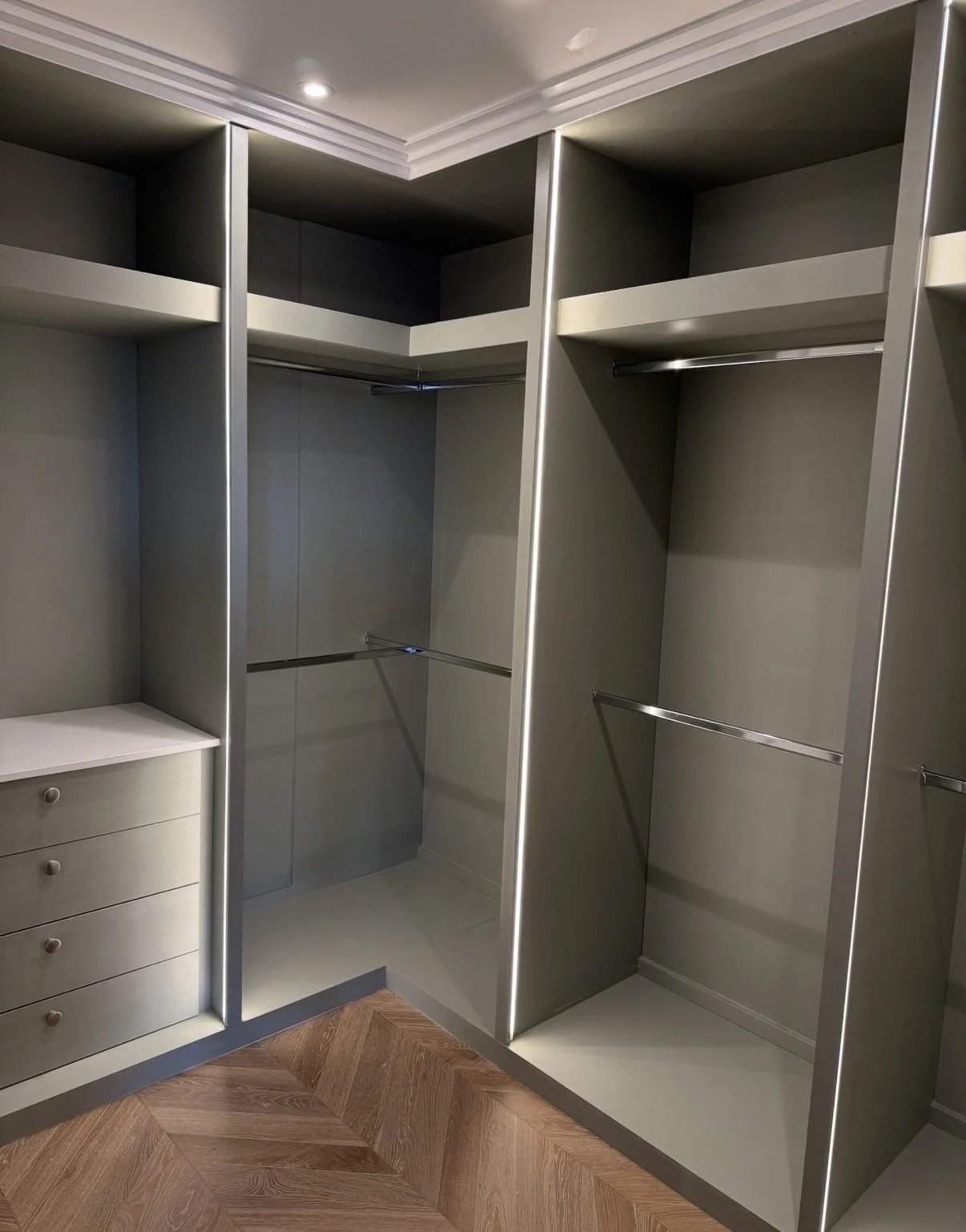 Empty walk-in closet with built-in shelves, hanging rods, and a small chest of drawers, illuminated by ceiling lights, with wooden flooring.