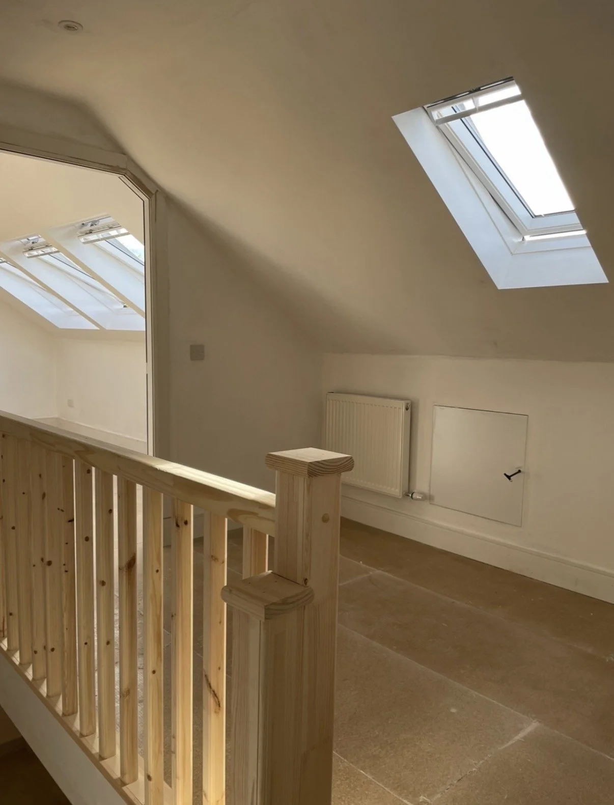 A cozy attic with a sloped ceiling, wooden railing, and two skylight windows allowing natural light.