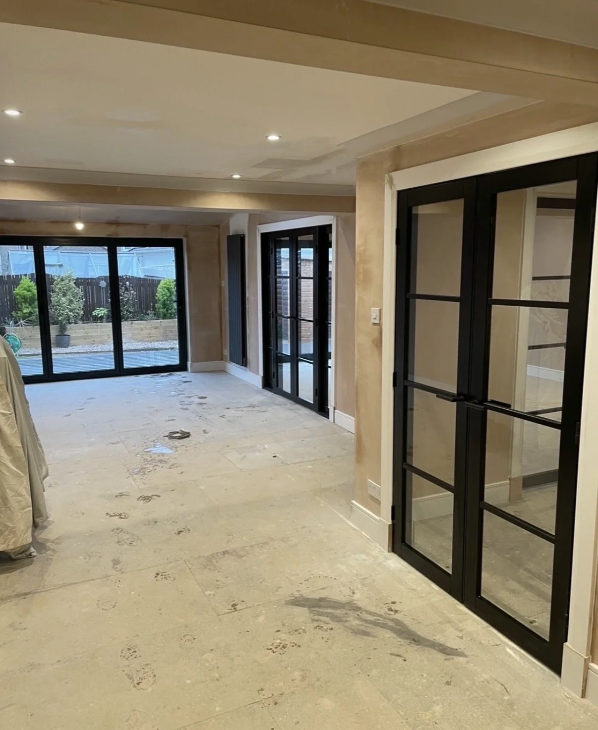 Interior of a house under renovation with sliding glass doors leading to a backyard, and newly installed black-framed glass doors dividing rooms.