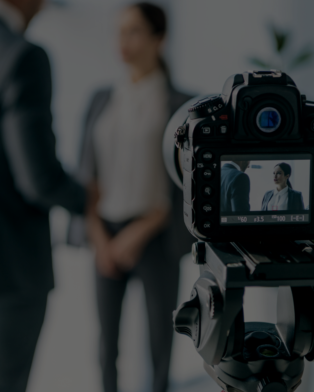 A professional camera capturing a photo of a man and woman in business attire, blurred in the background.