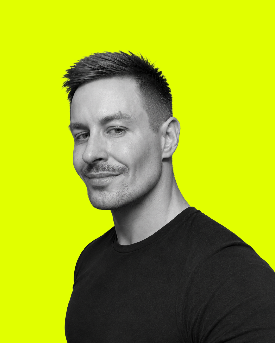 A black and white portrait of a man with short hair, smiling slightly, wearing a black shirt, against a bright yellow background.