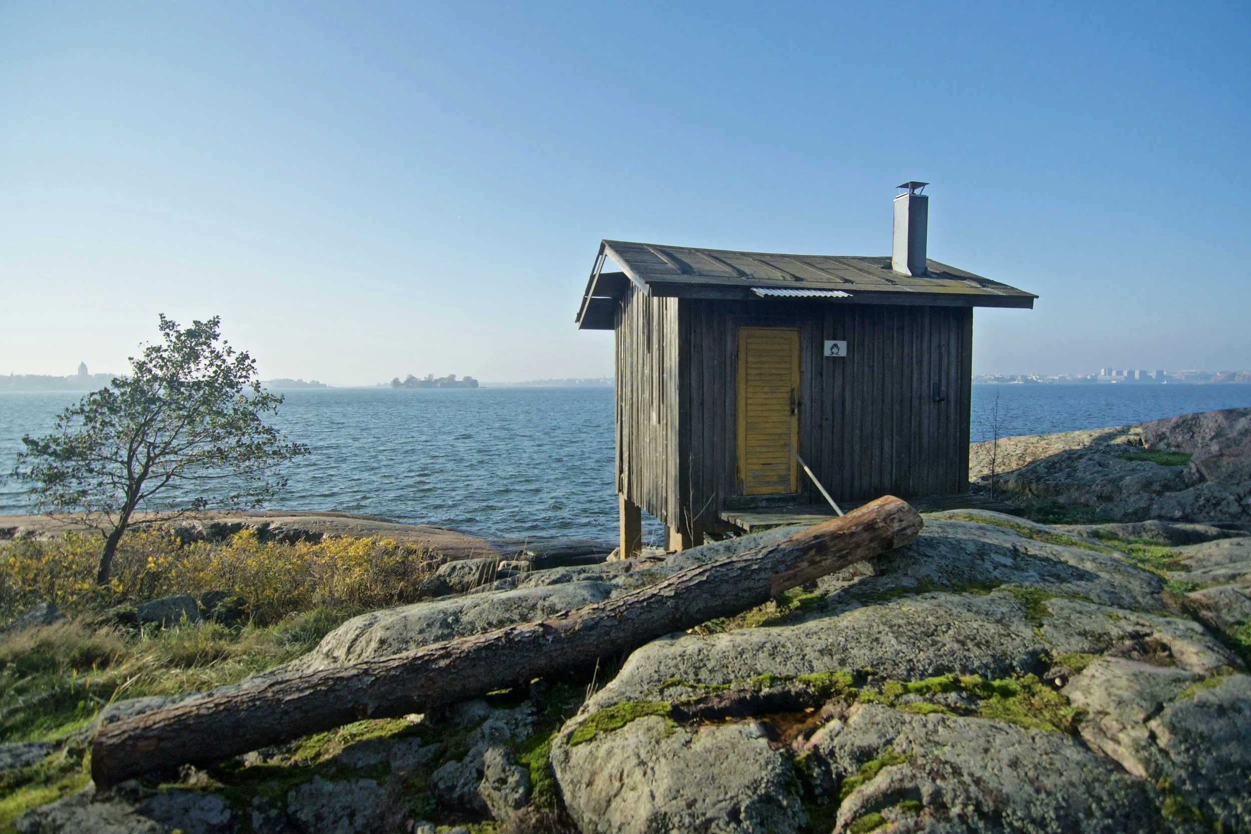 A wooden house overlooking a body of water with a clear blue sky in the background.