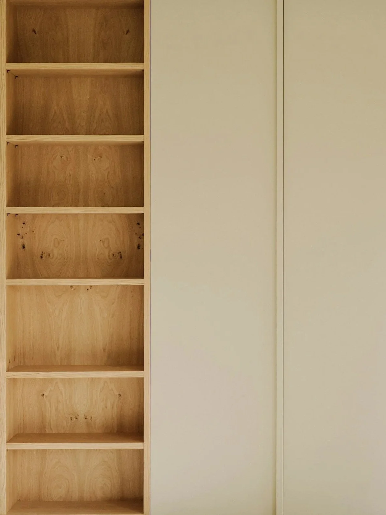 Empty wooden bookshelf with seven shelves next to a plain, cream-colored wall.