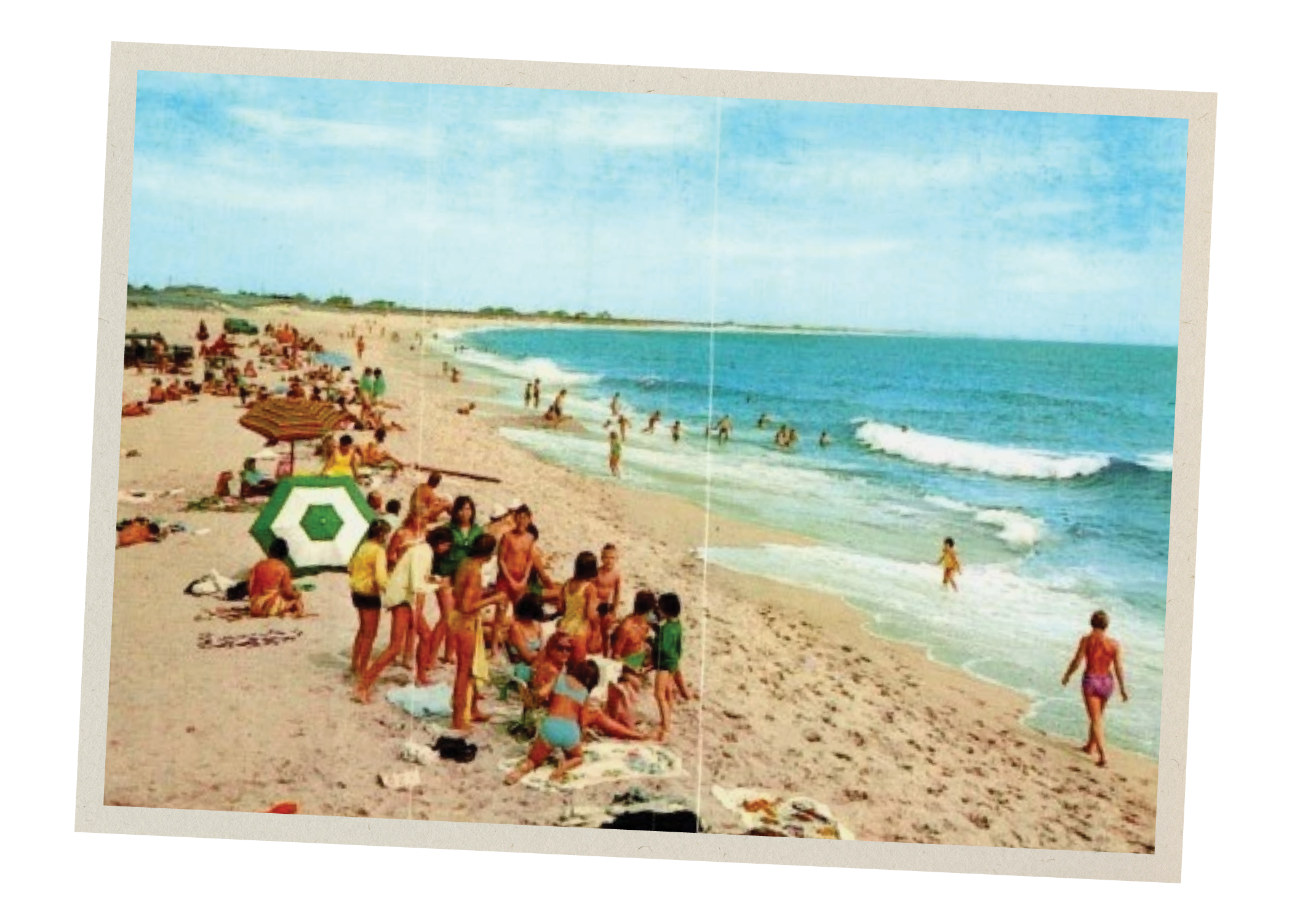 A vintage photograph of a crowded beach scene with many people sunbathing, walking, and playing near the shoreline under a partly cloudy sky.