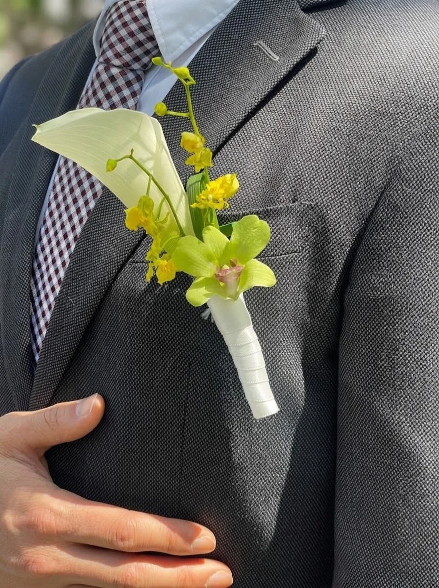 A boutonni&egrave;re, with a little edge.

Lime green, vivid yellow and sculptural movement &mdash; designed to sit against the quiet structure of a charcoal suit.

Rather than an afterthought, the groom&rsquo;s boutonni&egrave;re becomes part of the