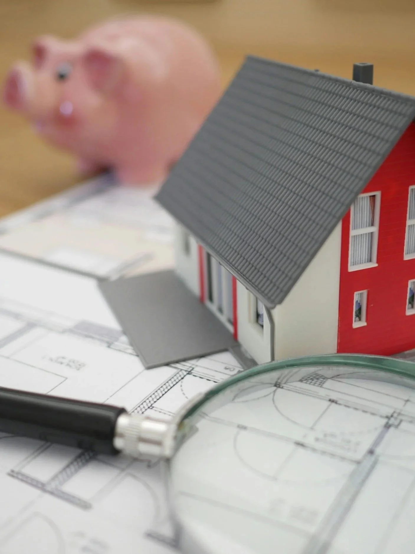 Close-up of a small architectural model of a house with a gabled roof, placed on architectural blueprints, with a black marker pen nearby.