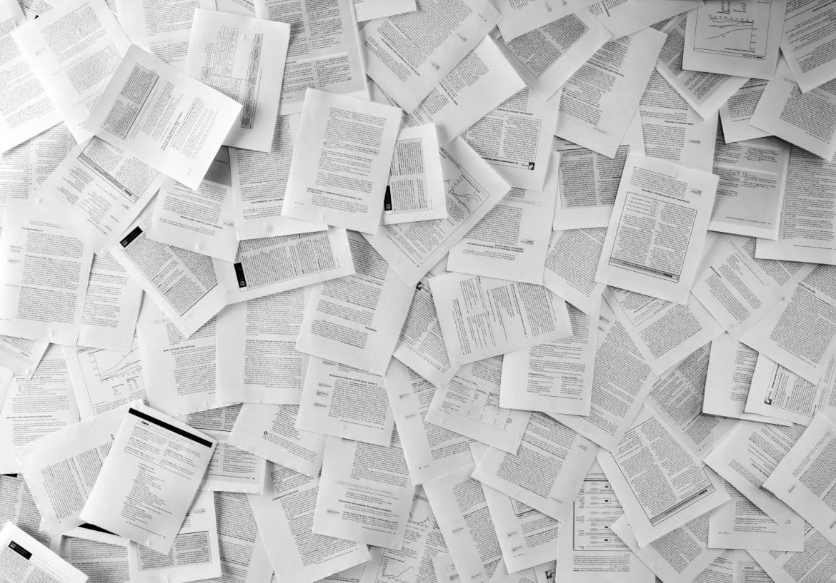 A large pile of scattered papers and documents on a flat surface, with various text and graphs visible.