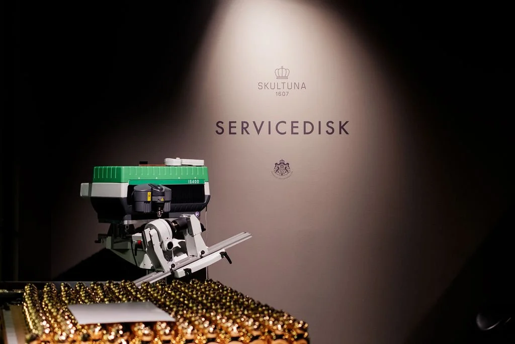 En maskindel med en vagn och en staty av en krona, texten skultuna och servivedisk i bakgrunden.