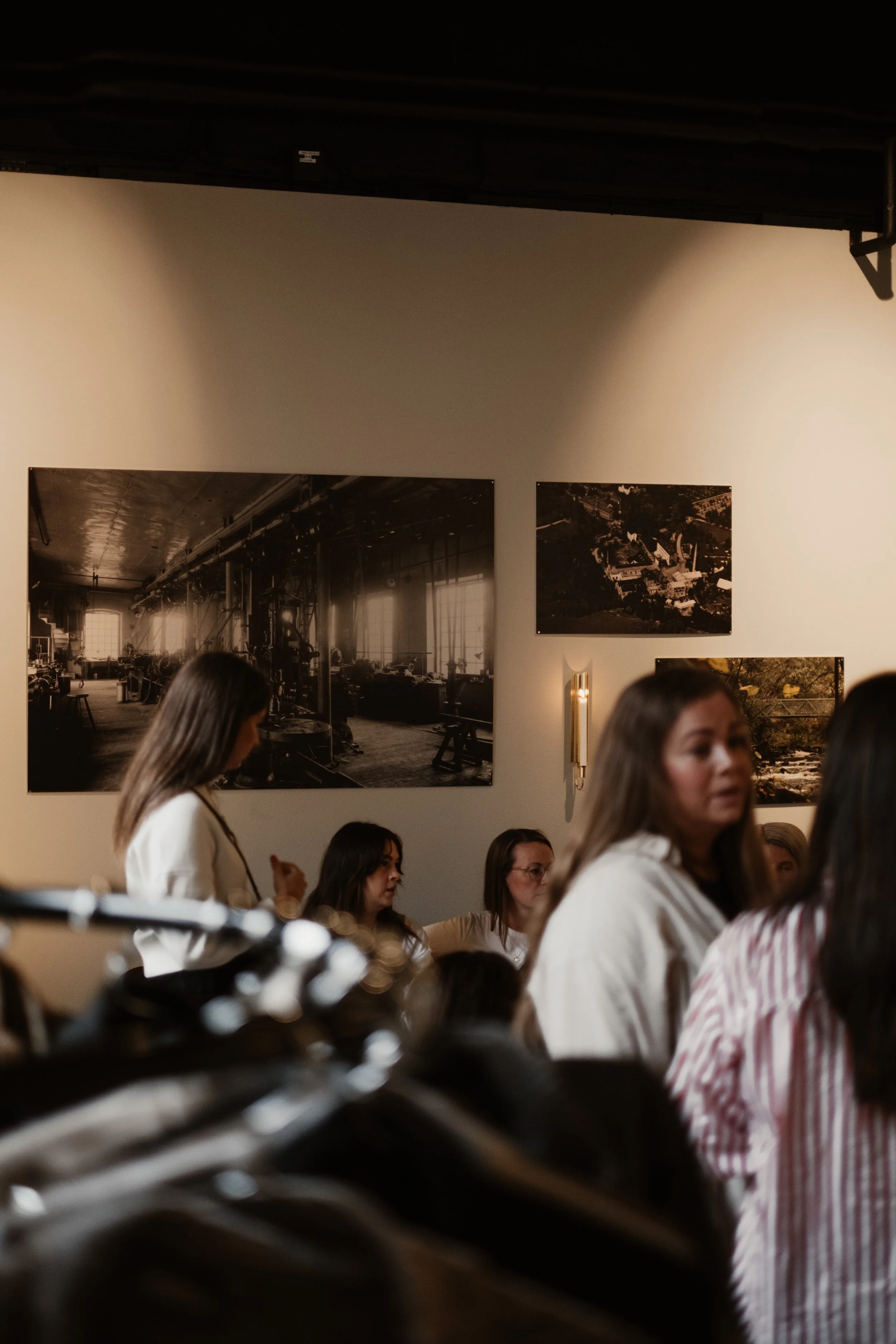 Interiörbild av ett galleri eller museum med fotografiska konstverk på väggarna. Flera personer, huvudsakligen kvinnor, samlas och pratar. Det är en social atmosfär med fokus på konst och samtal.