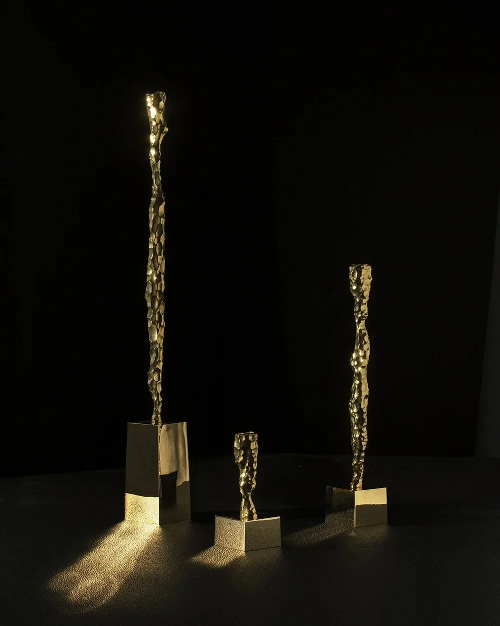 Tre guldfärgade skulpturer med en textured, hållbar design på mörk bakgrund.