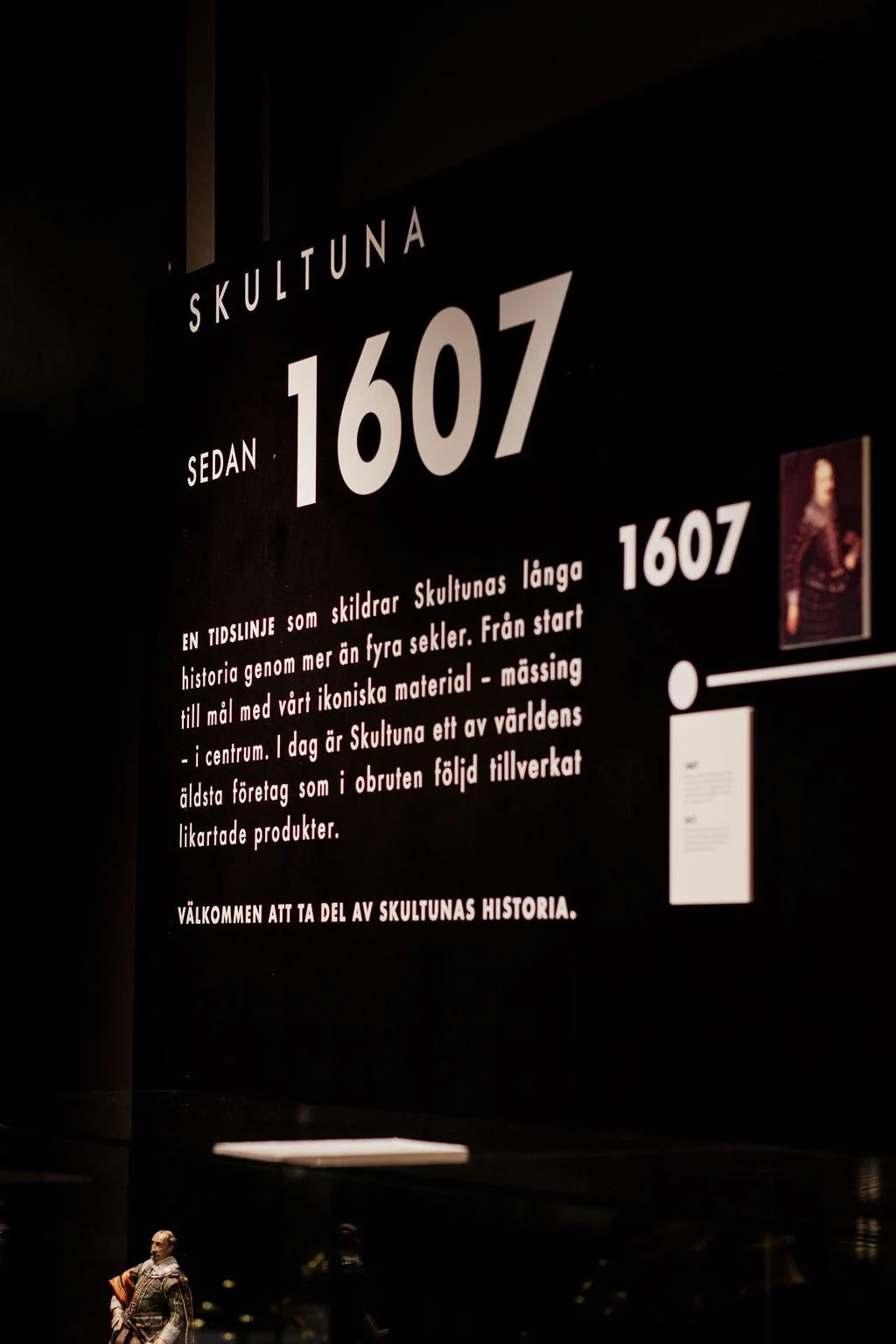Informationsskylt om Skultuna, med text som förklarar dess långa historia och ikoniska material, samt en liten bild av en person i traditionell klädsel.