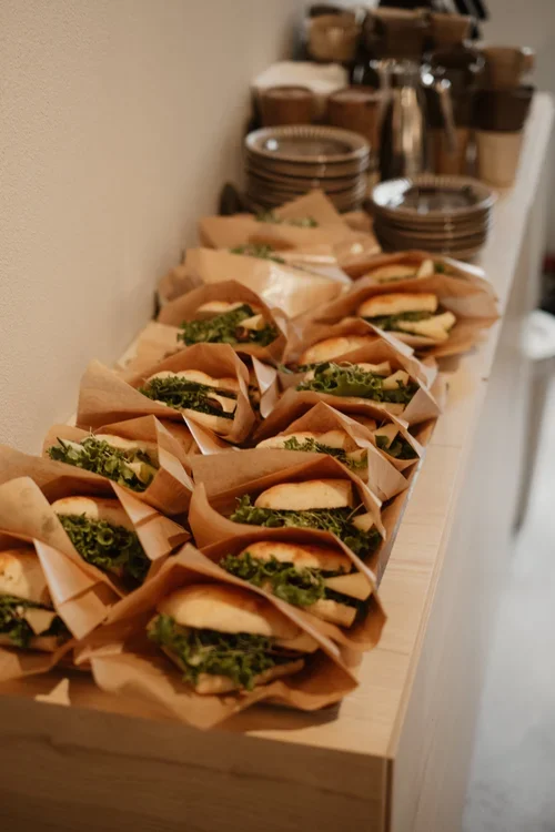 Flera sandwichar med grönsaker, inlindade i brunt papper, placerade på ett lätt träbord.