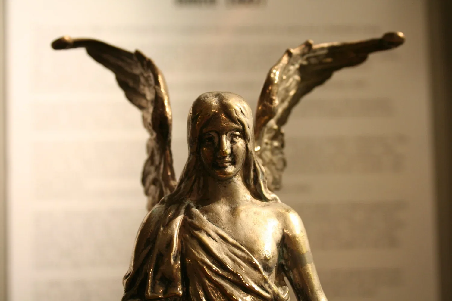 En guldfärgad skulptur av en kvinnlig figur med vingar, som står mot en ljus bakgrund.