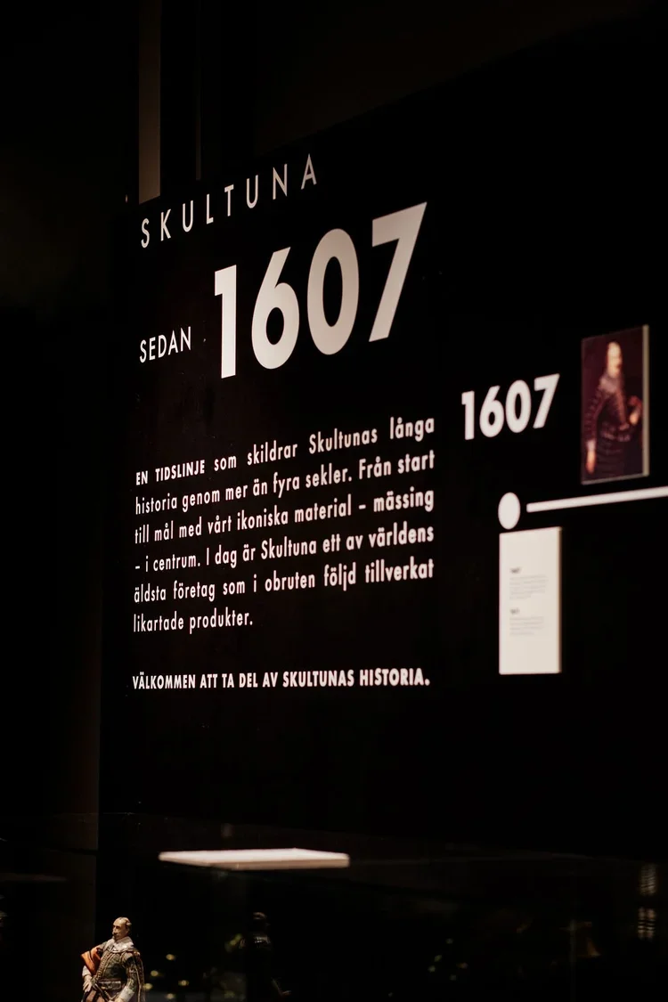 Informationsskylt om Skultuna och dess historia sedan 1607, med en bild av en man i traditionell klädsel i botten av skylten.