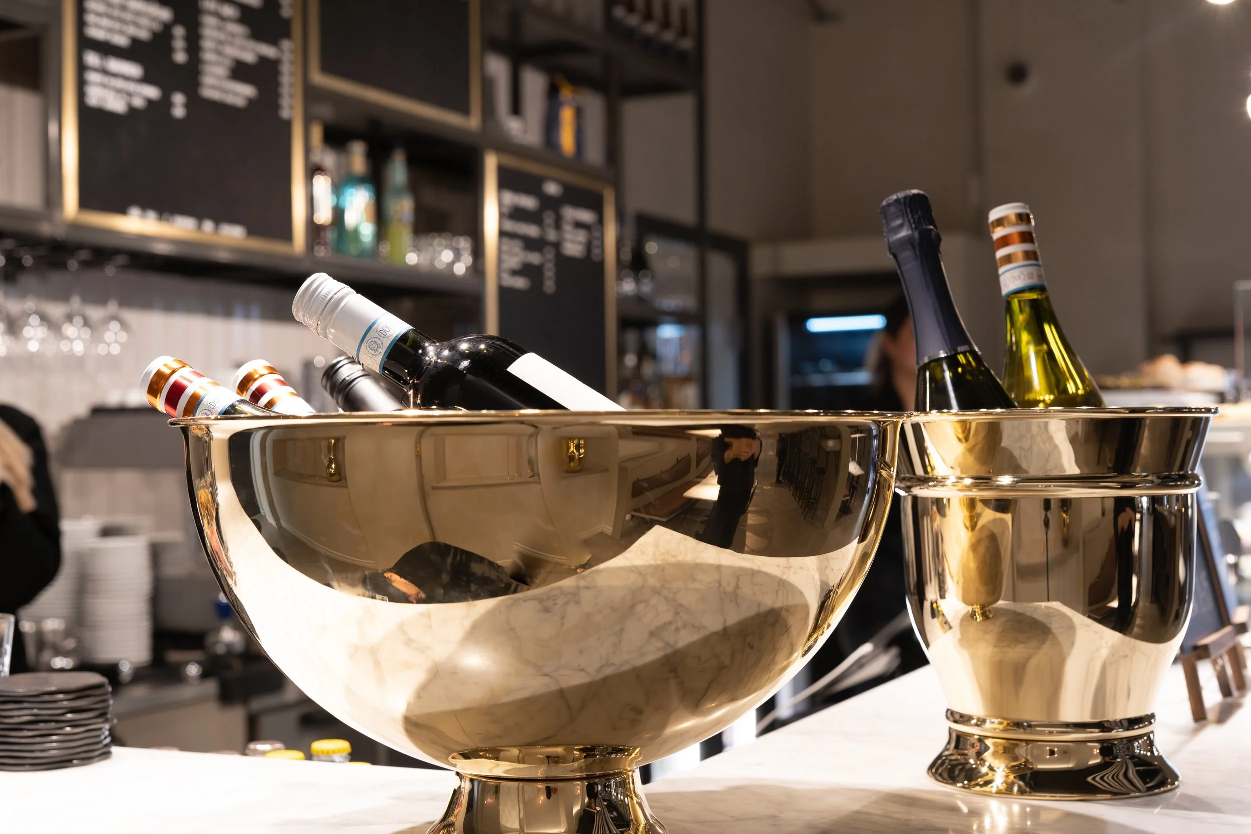 Guldfärgad skål med vinflaskor inne på ett café eller bar.