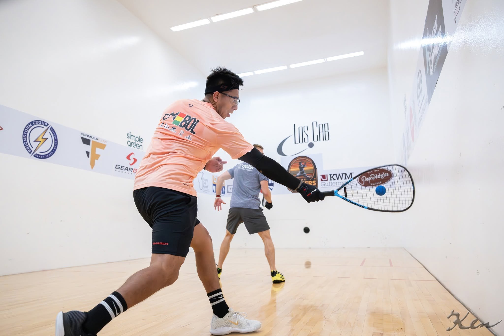 A man playing indoor pickleball with a paddle and ball, wearing athletic clothing while running on a court.