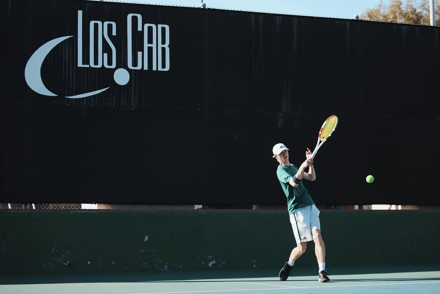 A man and woman playing tennis on a rooftop court, with city buildings in the background.
