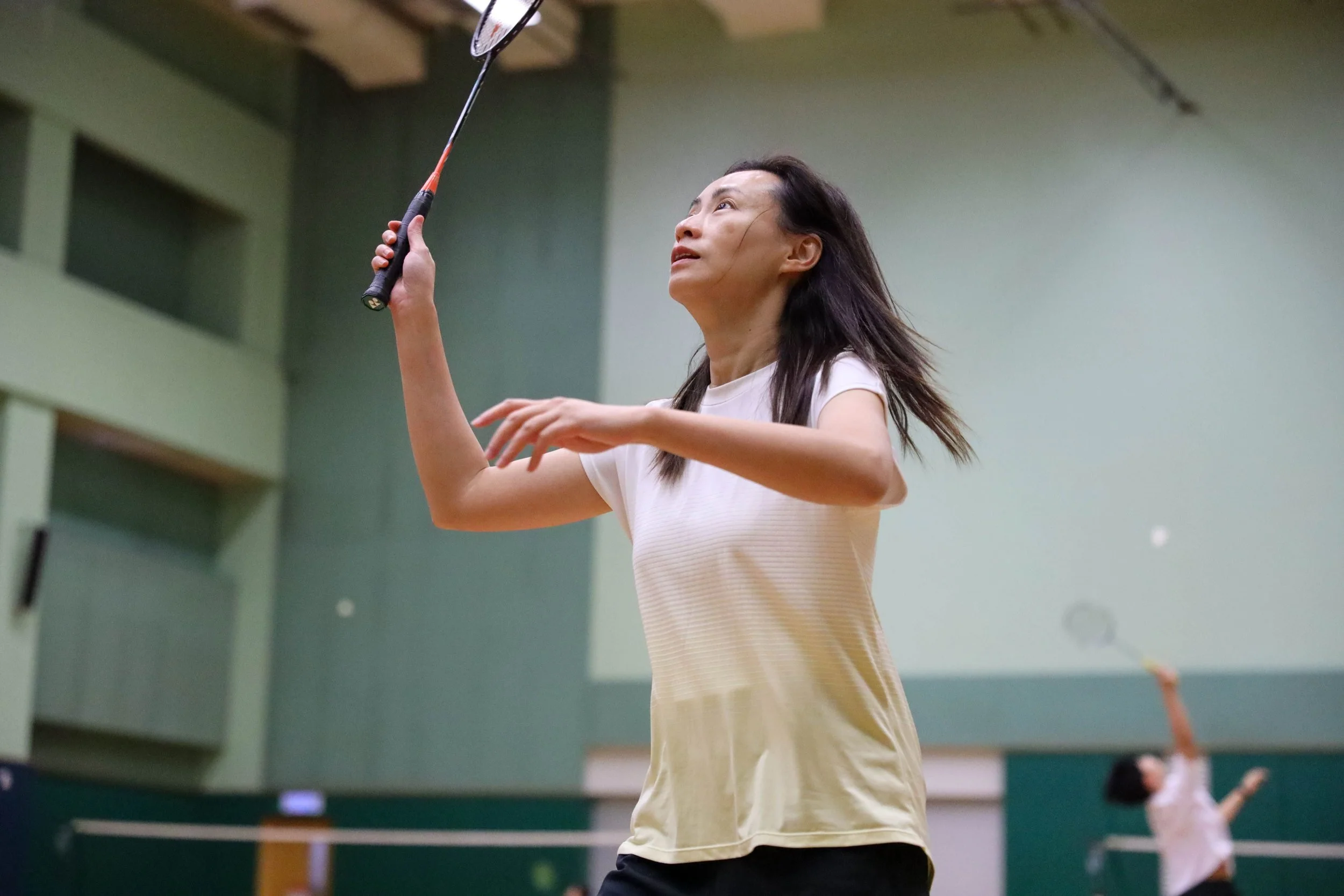 Woman playing badminton indoors, holding a racket and preparing to hit a shuttlecock.