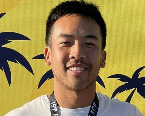 Young man smiling in front of a yellow background with black palm trees