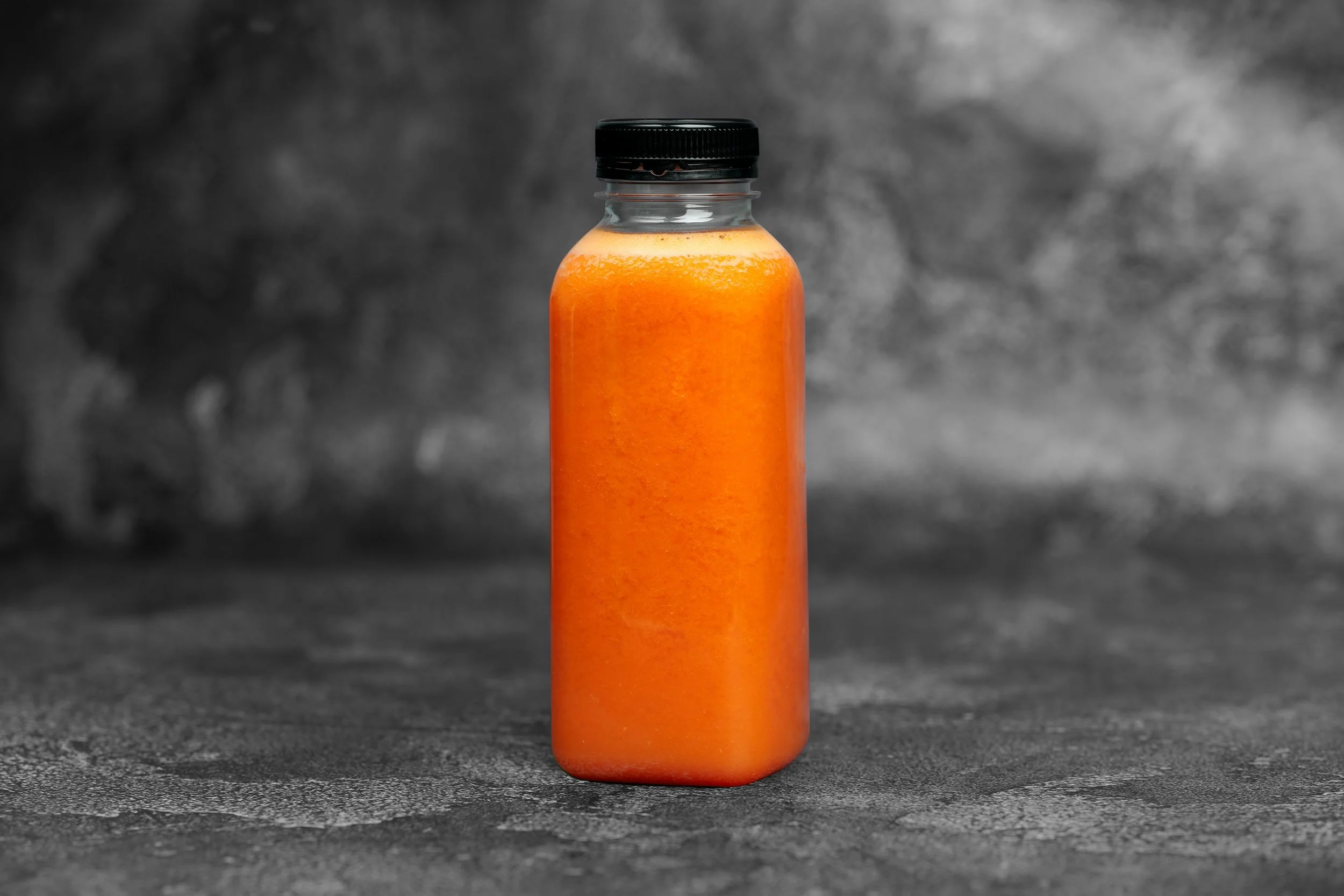 A small orange bottle with a black cap on a textured gray surface with a blurred dark background.