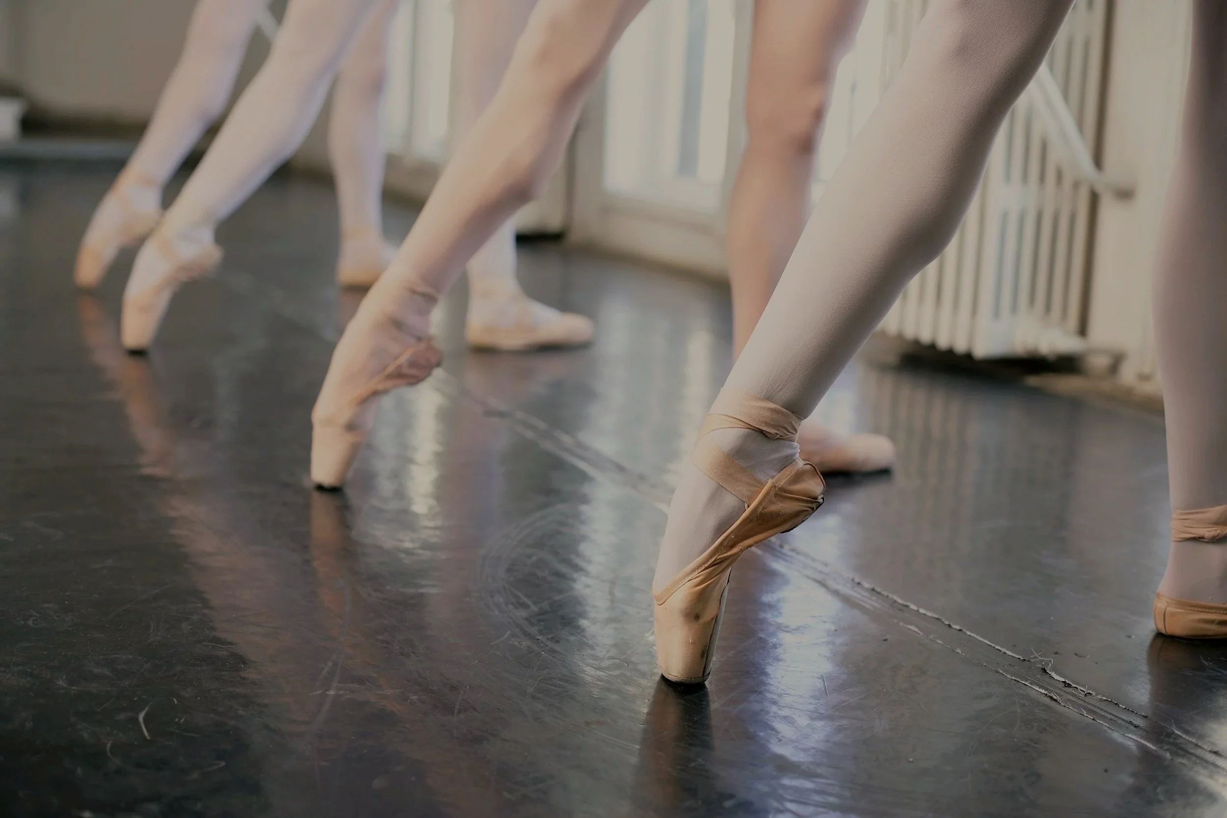 Close-up of ballet dancers’ feet in pointe shoes during practice.