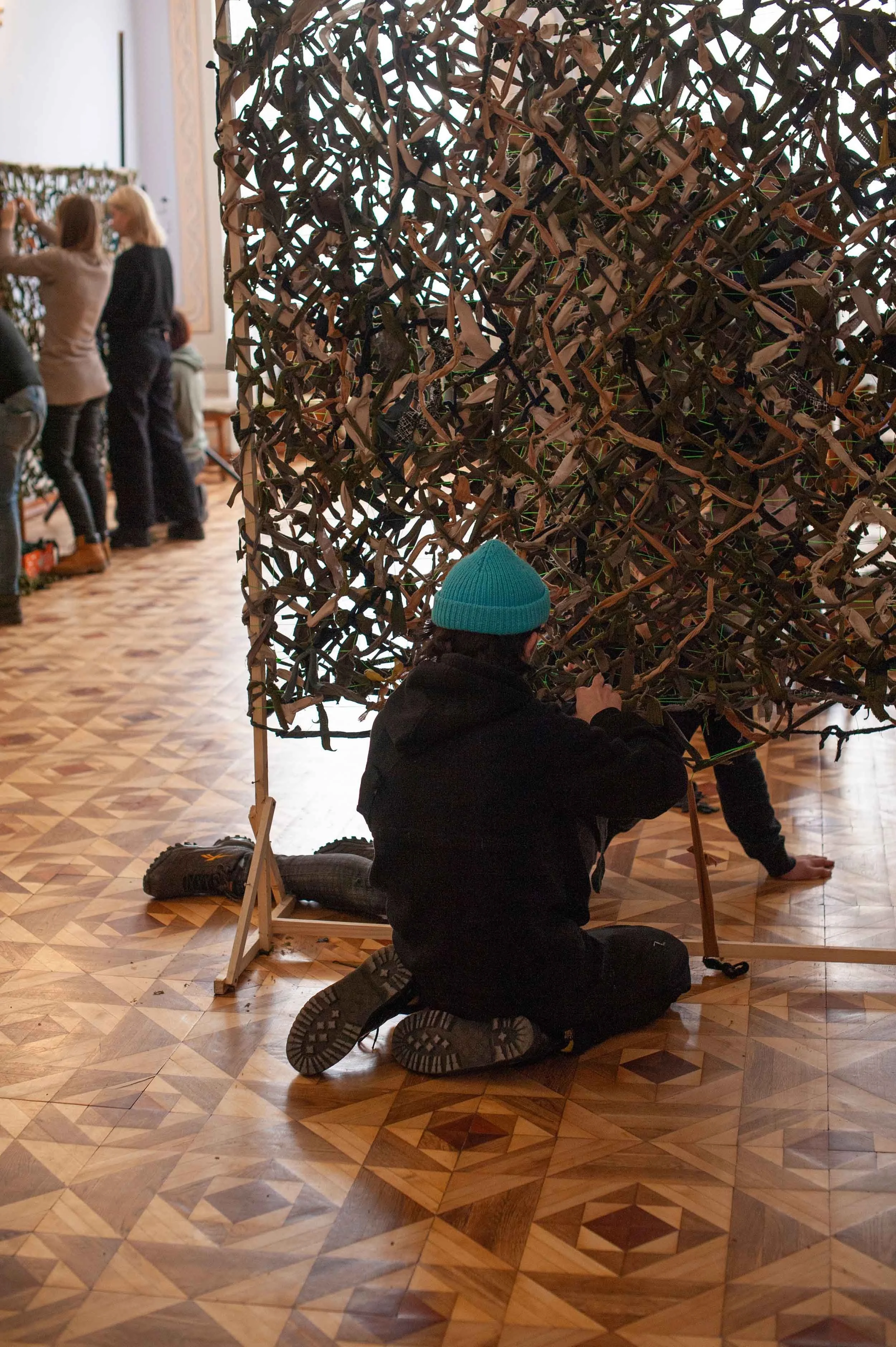 People assembling a large woven installation in a gallery space.